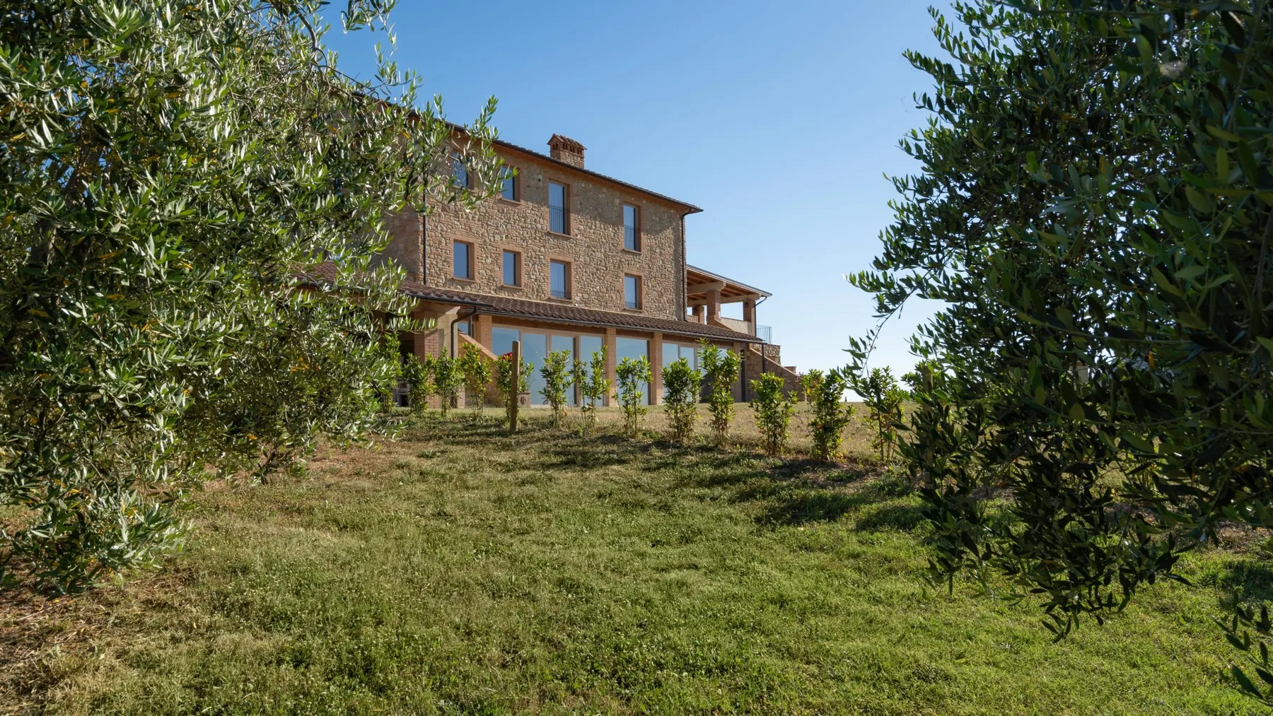 A multi-story brick house stands on a grassy slope among trees.