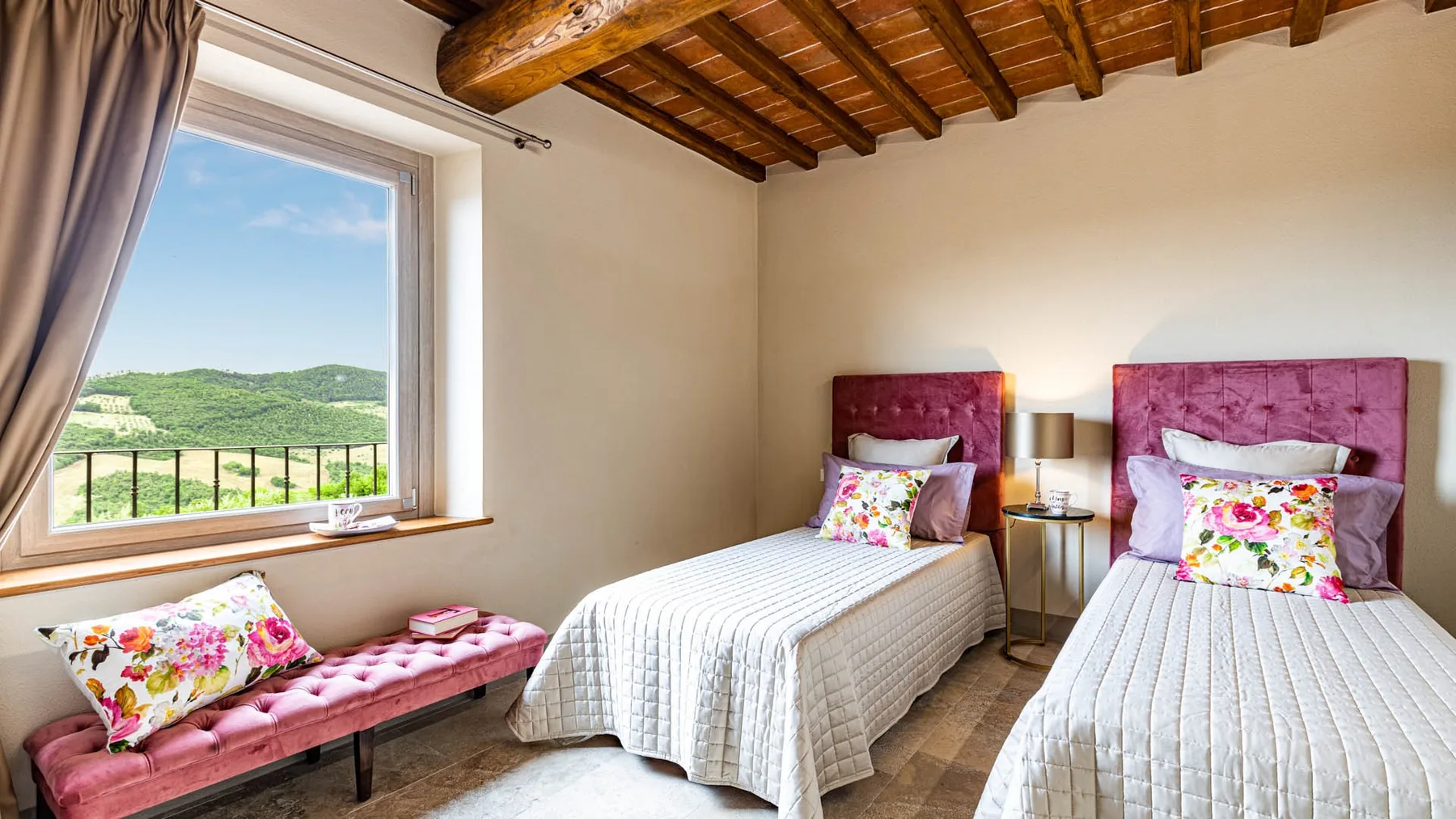 A twin bedroom with two beds, a window, and a view of green hills.