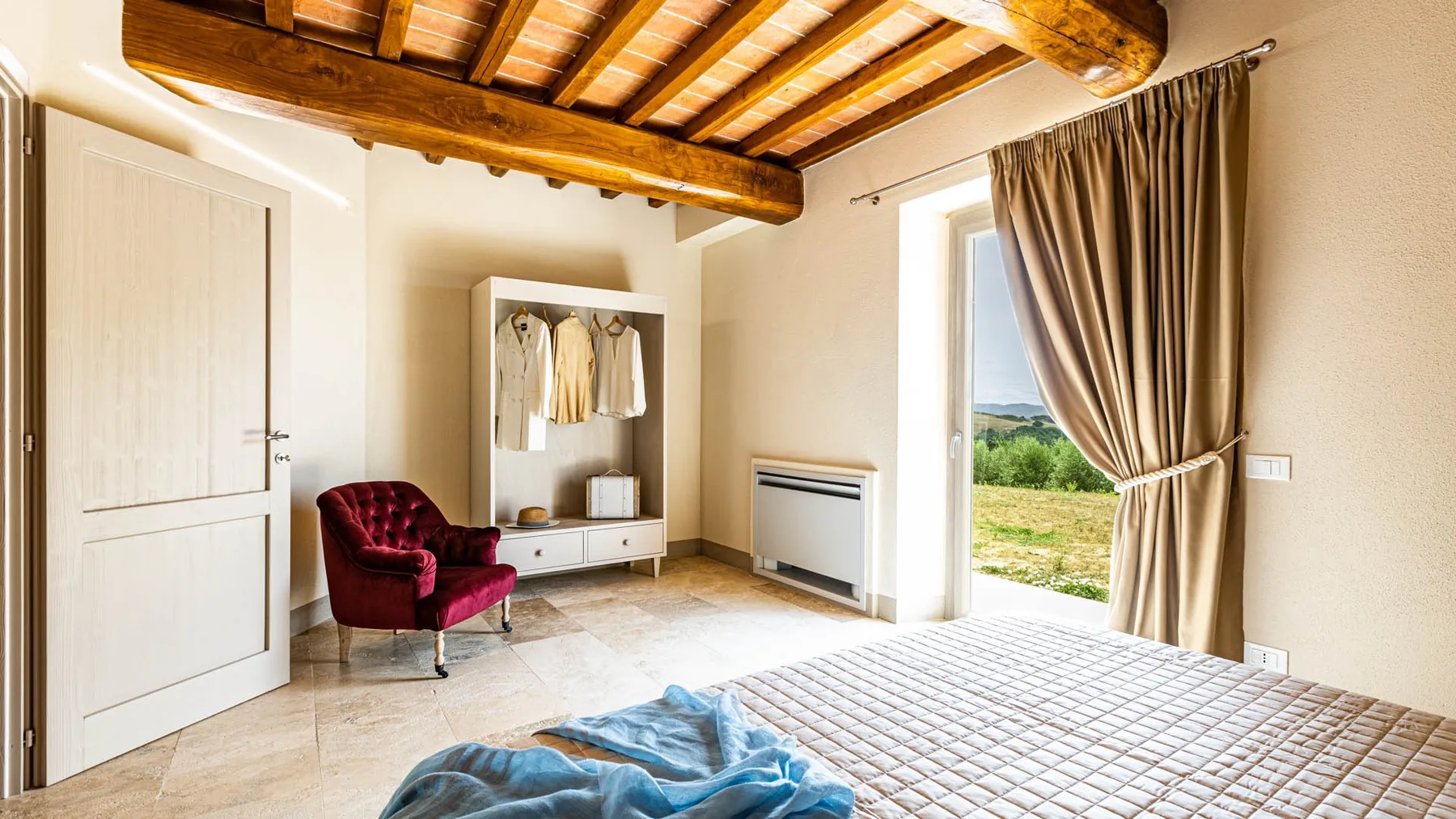 A bedroom with a bed, an open wardrobe, and a window overlooking greenery.