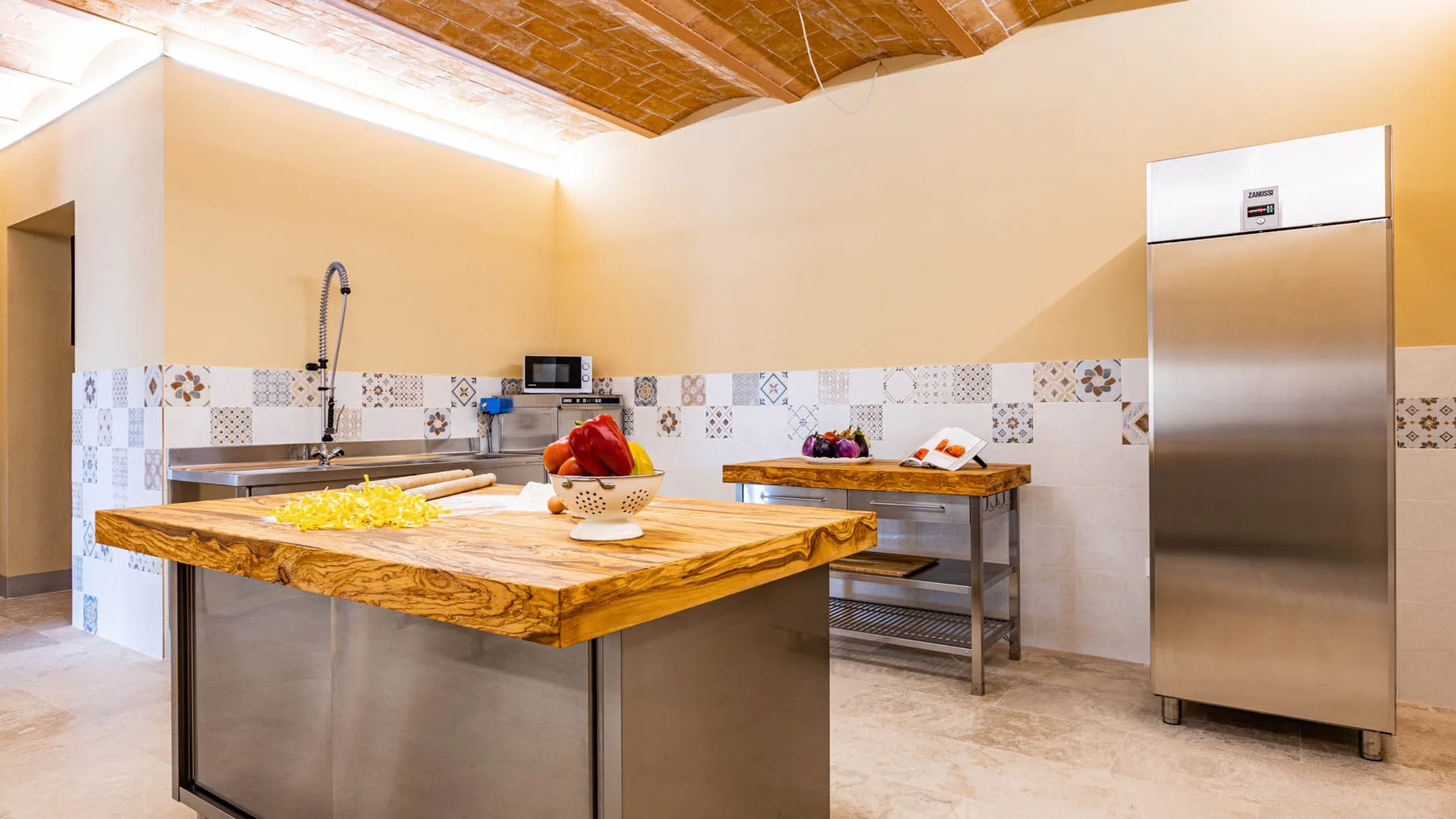 A spacious kitchen with a wooden island, tiled backsplash, and stainless-steel refrigerator.