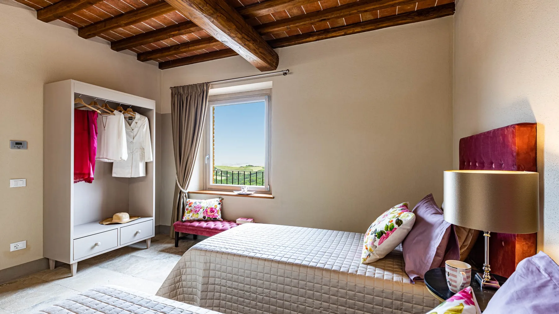 A bedroom with a bed beside a window and an open wardrobe.