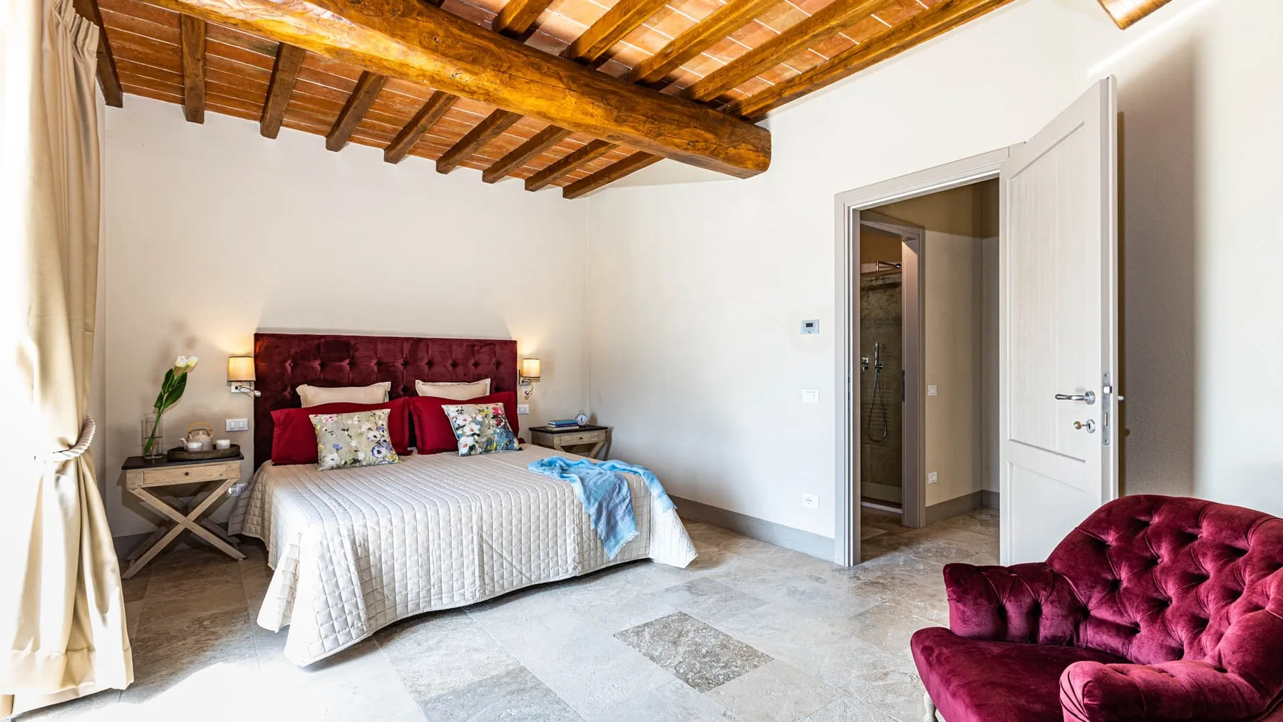 A bedroom with a bed, exposed wooden ceiling beams, and an open doorway.