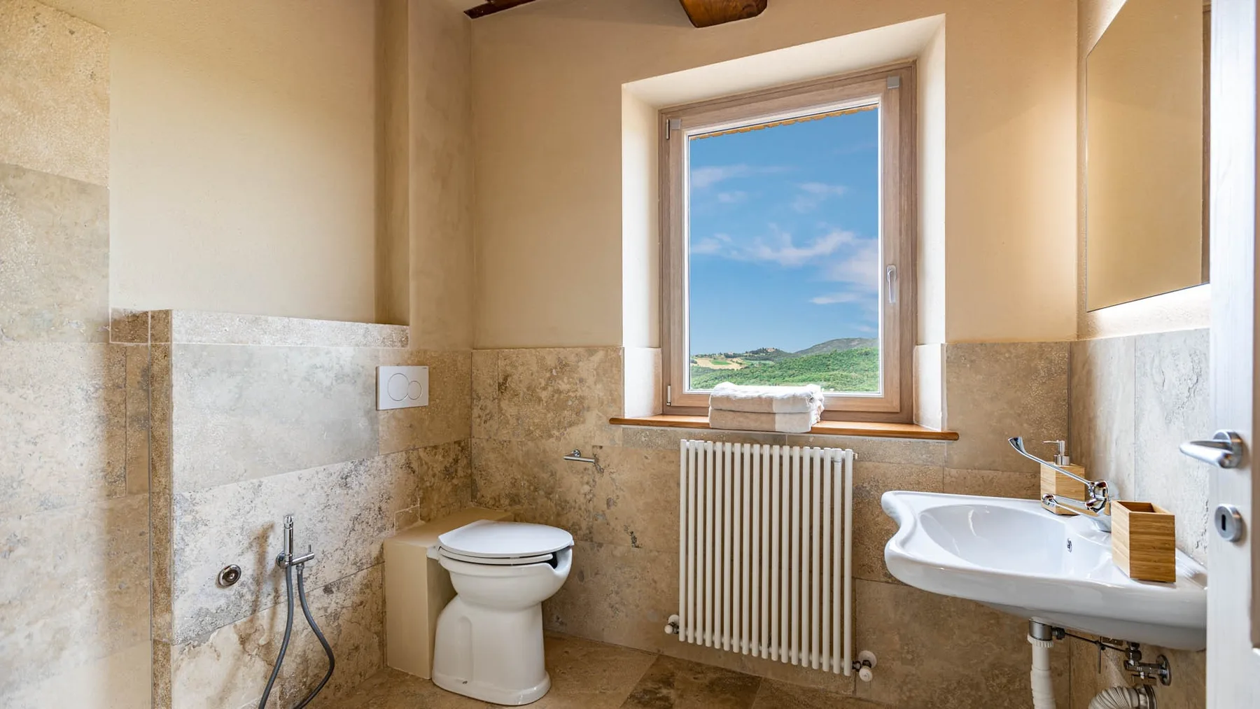 A bathroom with a toilet, sink, and window overlooking a green landscape.