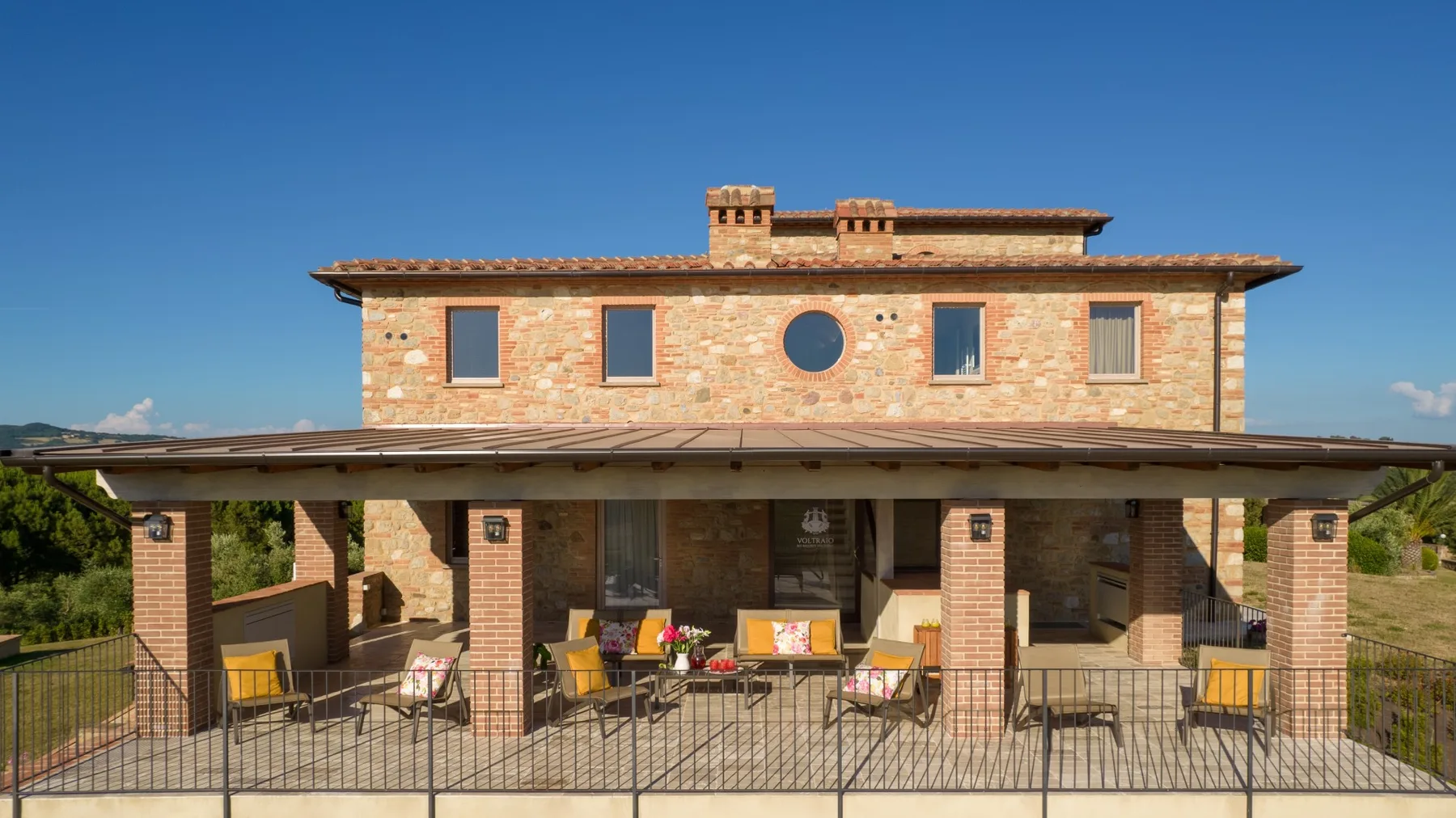 A brick house with a covered patio and outdoor seating under a clear blue sky.