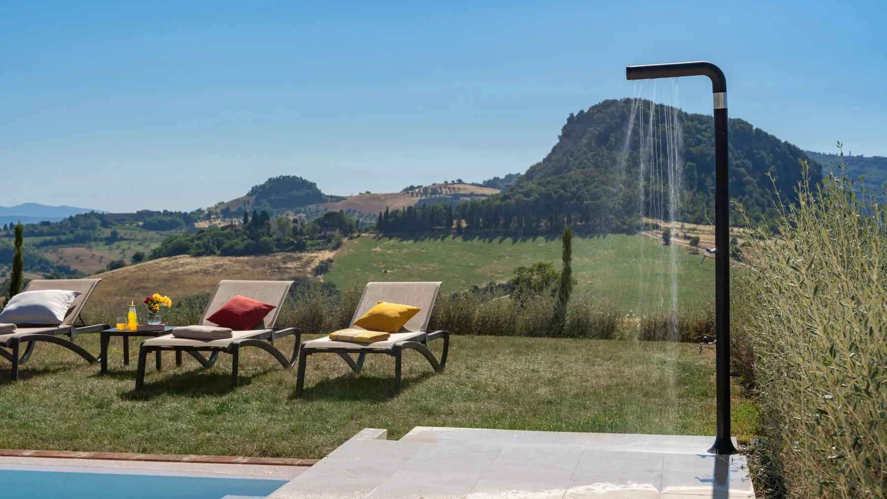 Outdoor poolside seating overlooks green hills beneath a clear blue sky.