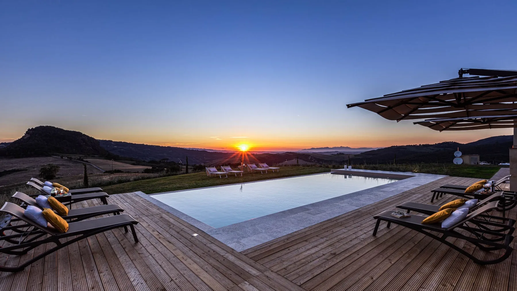 An outdoor pool and surrounding deck overlook a landscape at sunset.