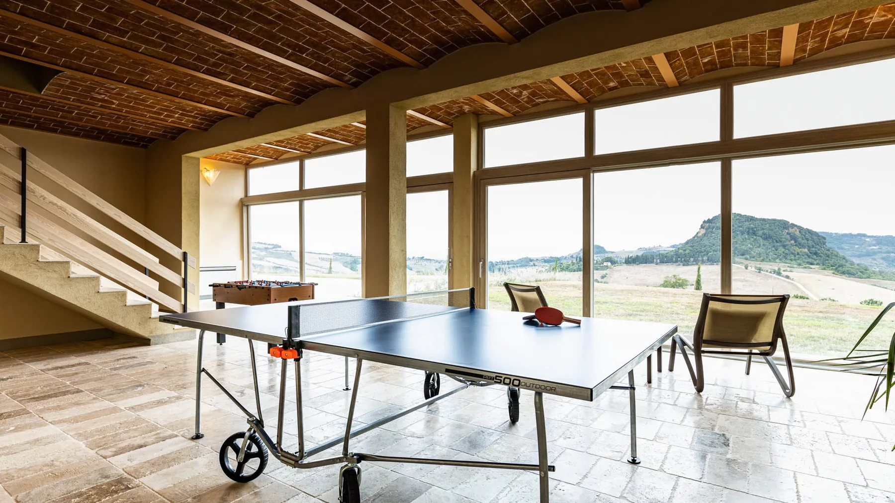 A bright recreation room with a table tennis table and large windows overlooking the landscape.