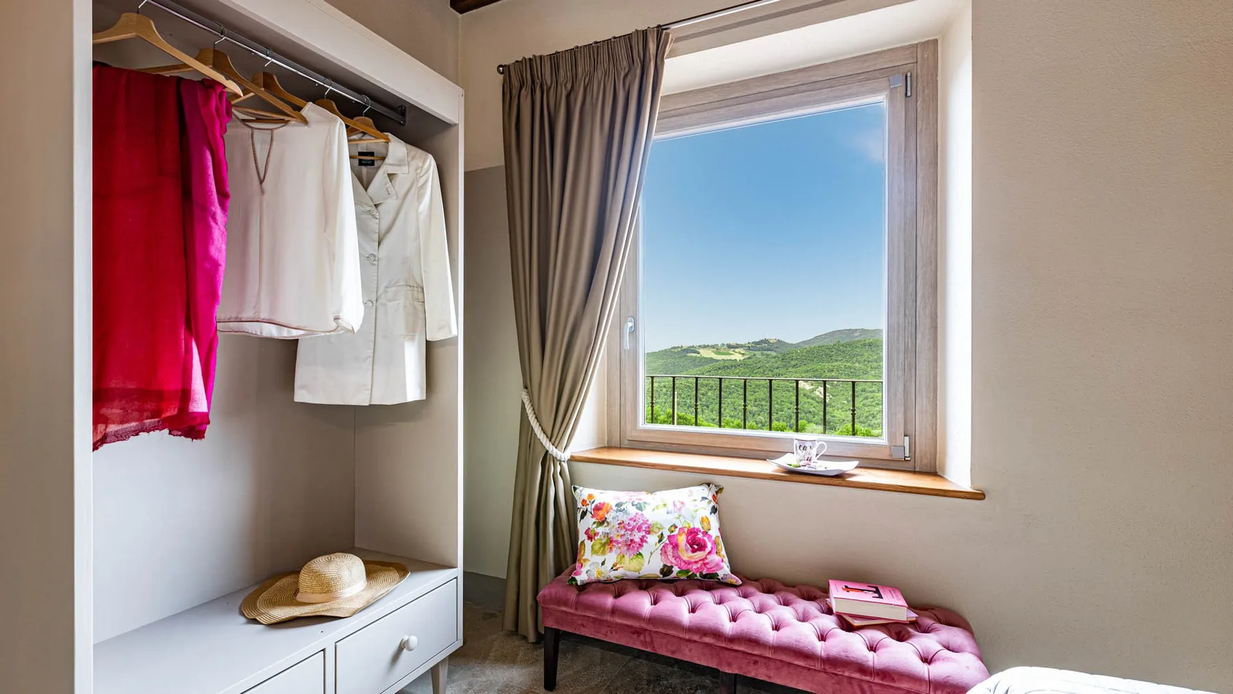 A bedroom window overlooks green hills, with a cushioned seat beneath it.