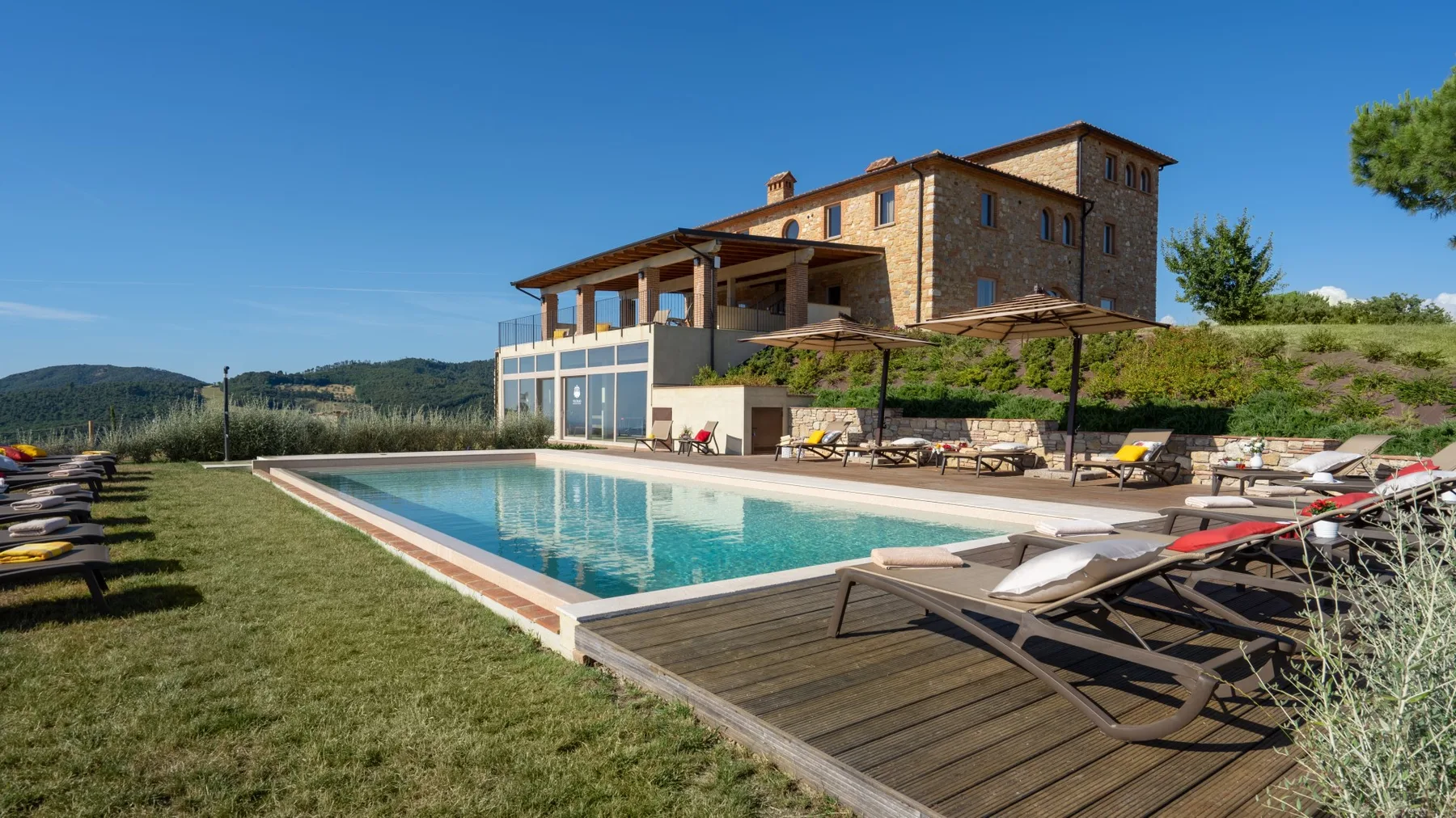 A stone countryside building overlooks a swimming pool and surrounding sun loungers.
