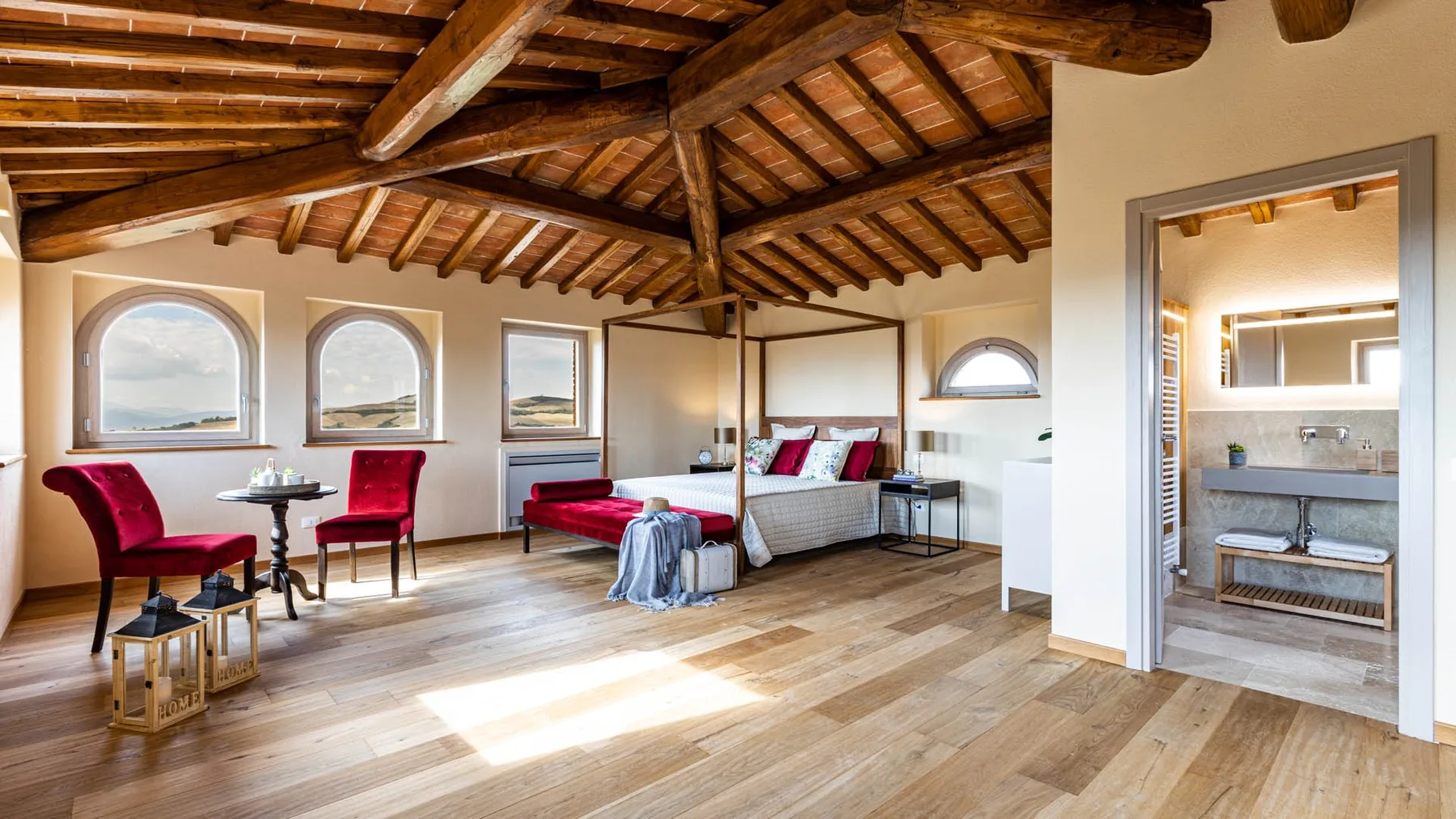 A bright bedroom with a bed, seating, and exposed wooden ceiling beams.