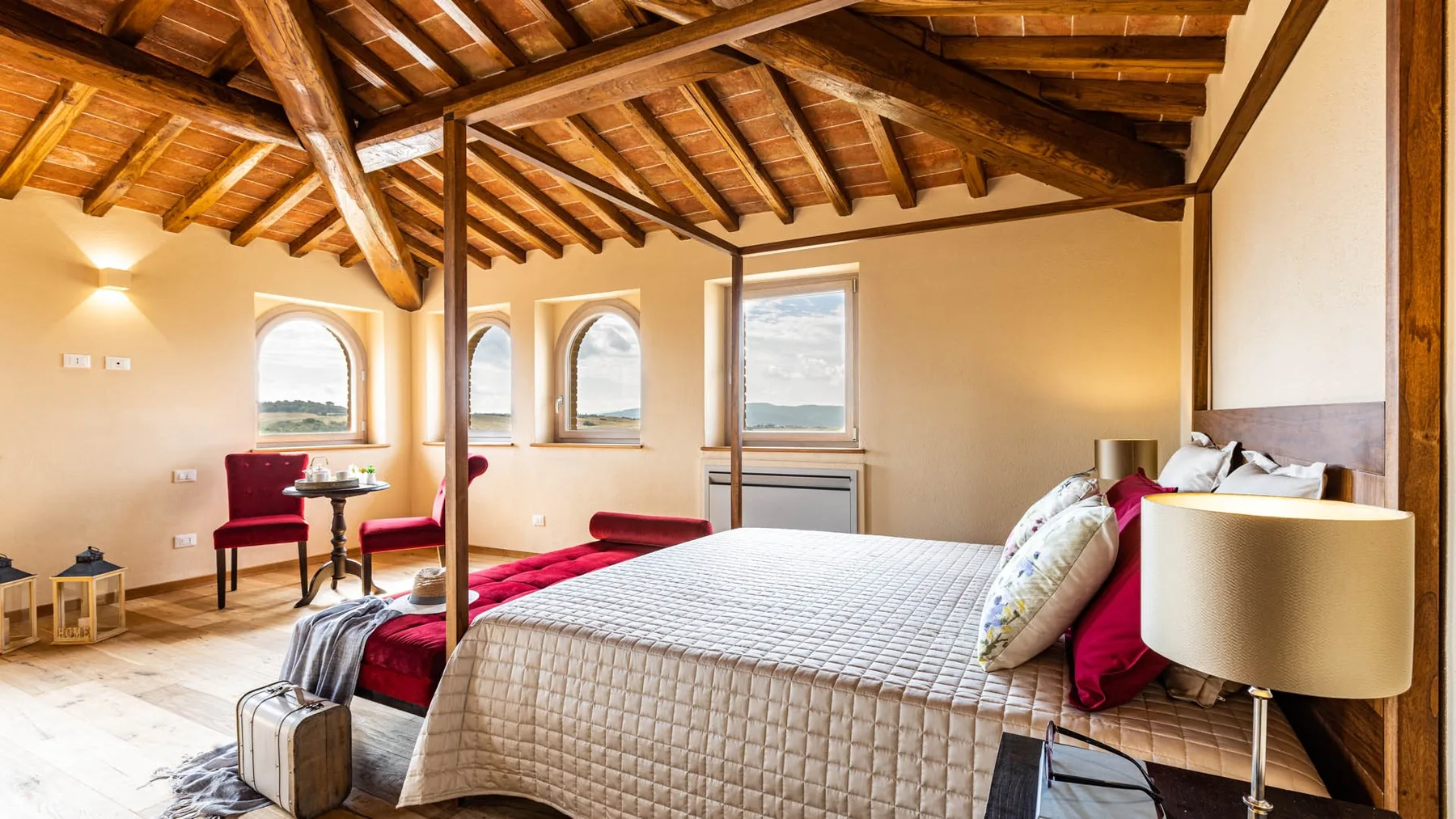 A bedroom with a large bed, exposed wooden ceiling beams, and arched windows.