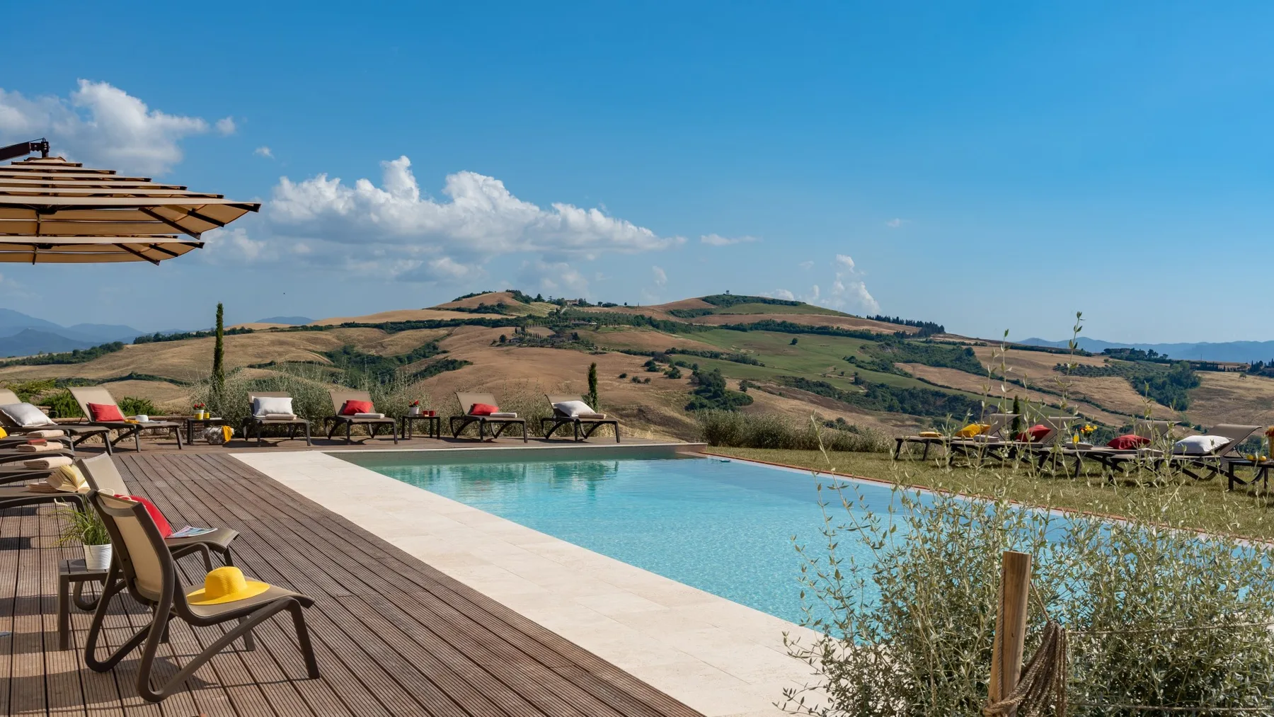 An outdoor swimming pool overlooks rolling hills, with seating along the wooden deck.