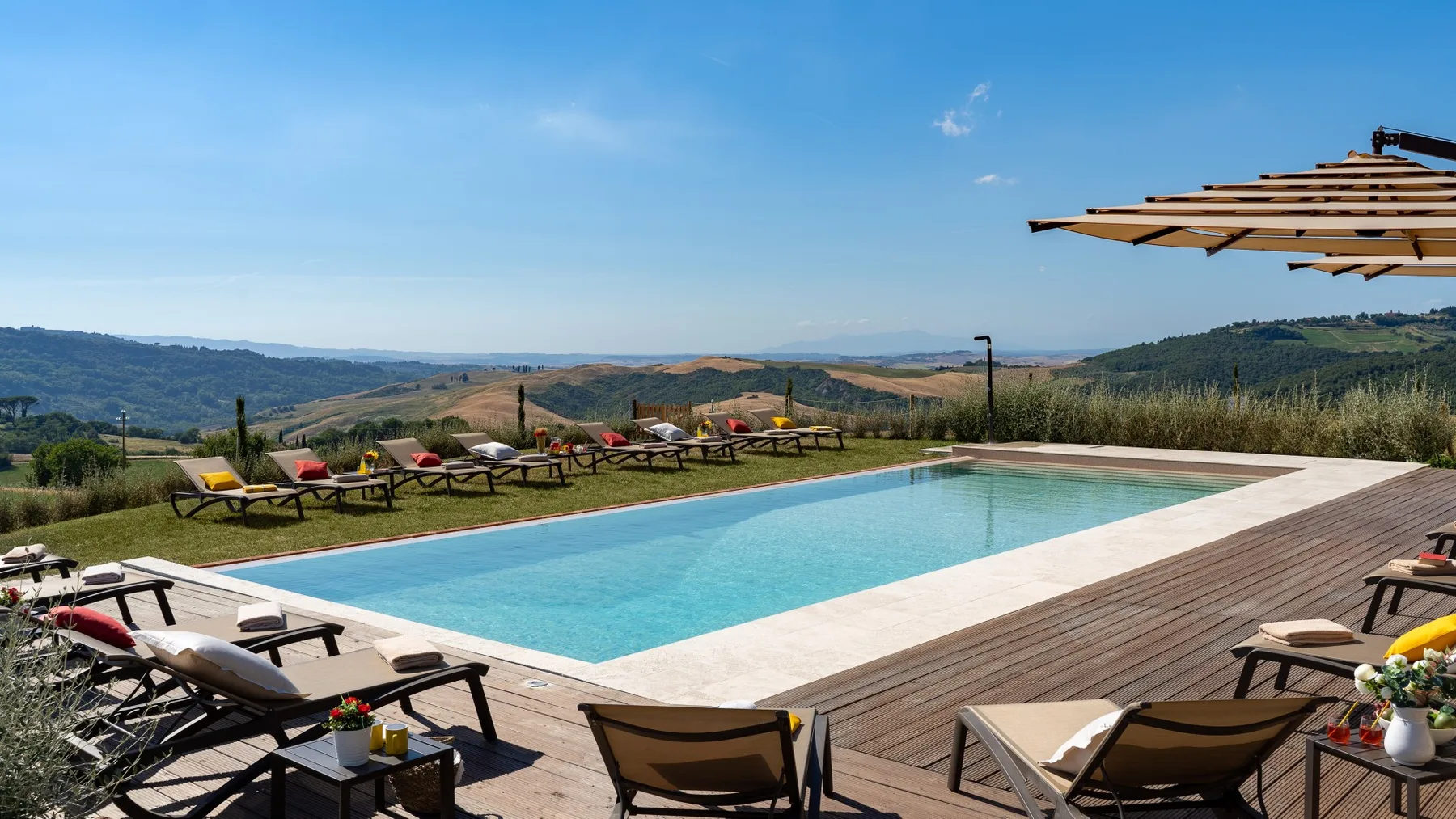 An outdoor swimming pool is surrounded by a wooden deck and lounge seating.