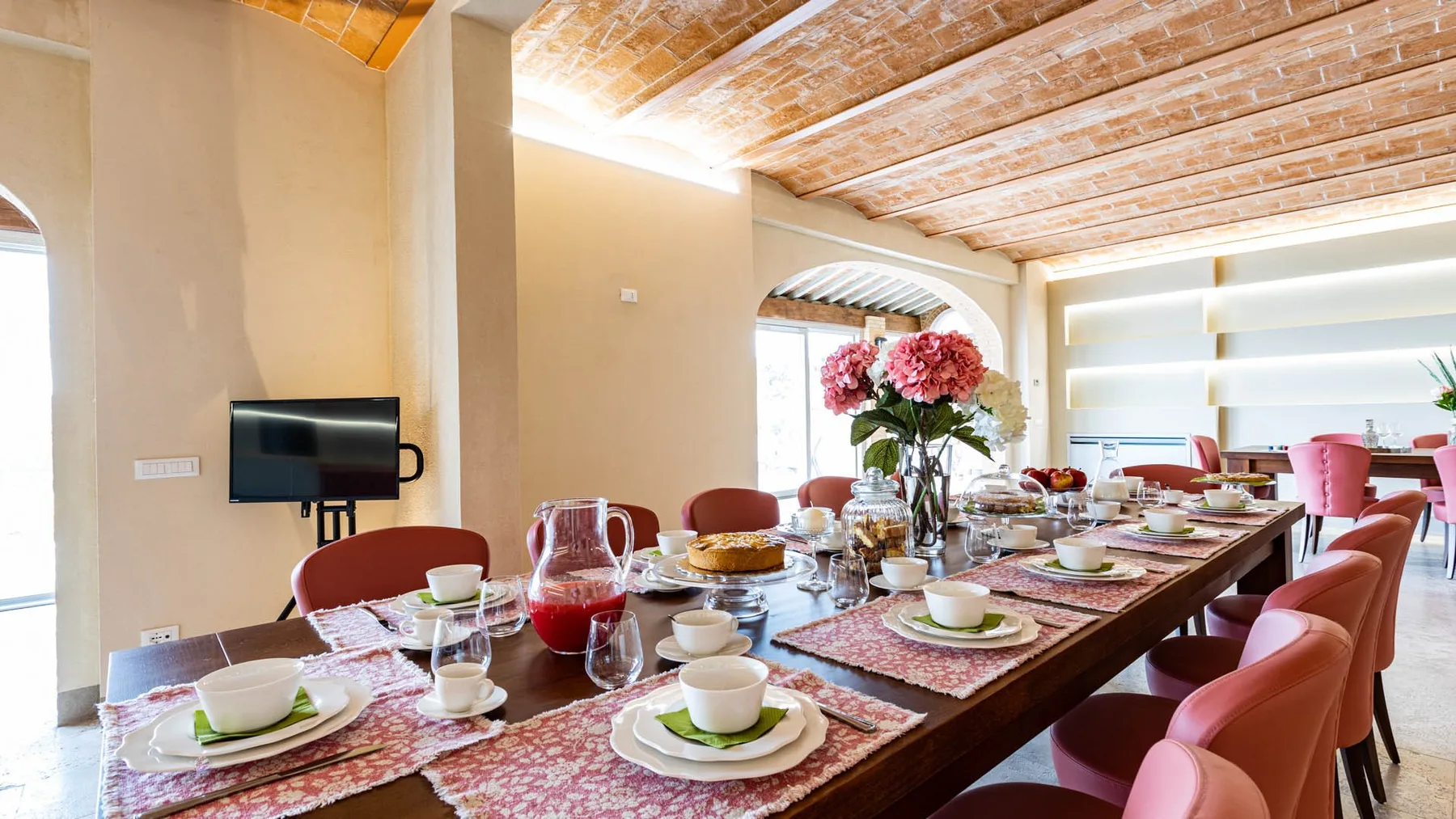 A dining room with a long table set with dishes and pink seating.