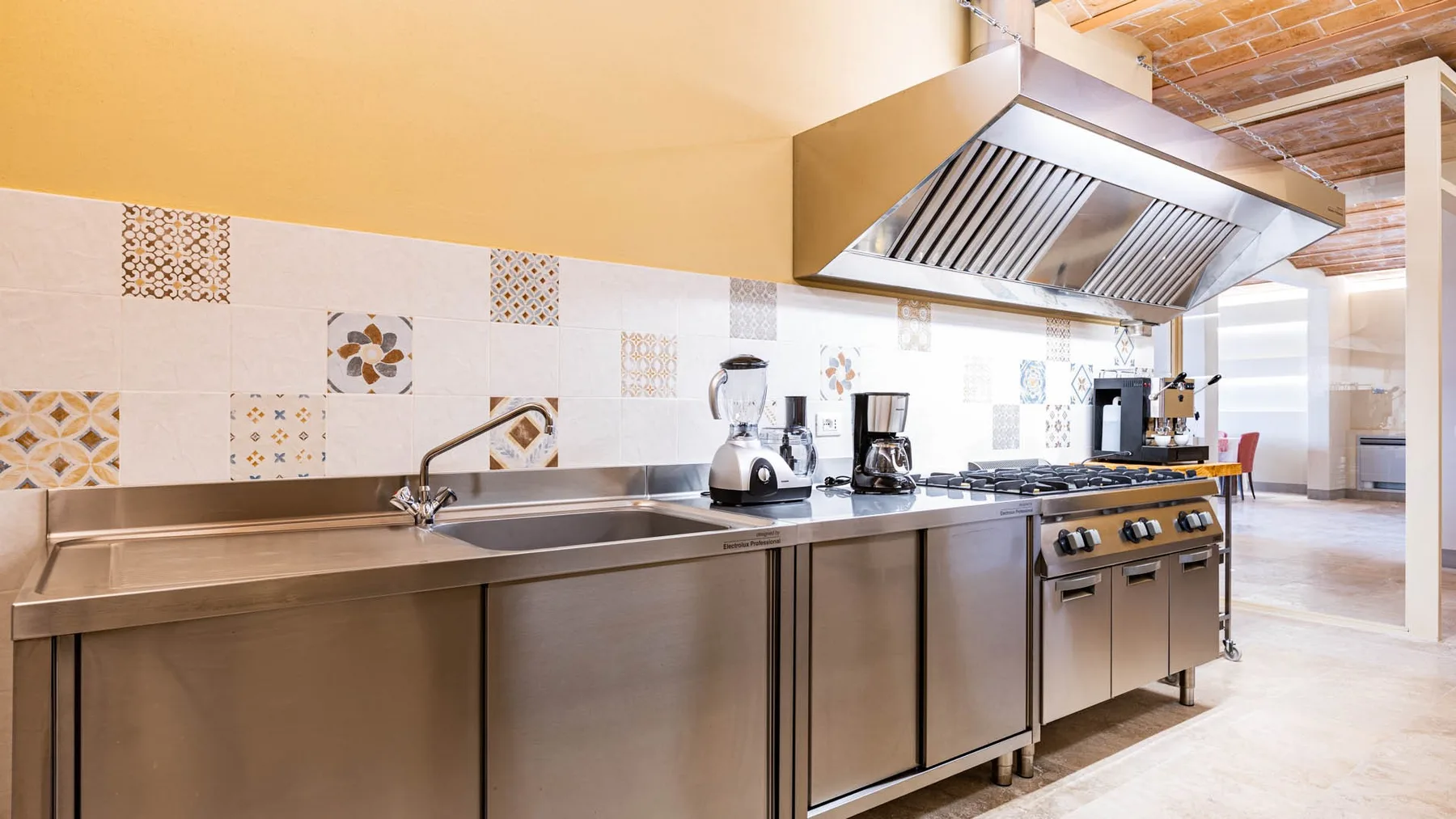 A commercial kitchen with stainless steel counters, cooking equipment, and a large ventilation hood.