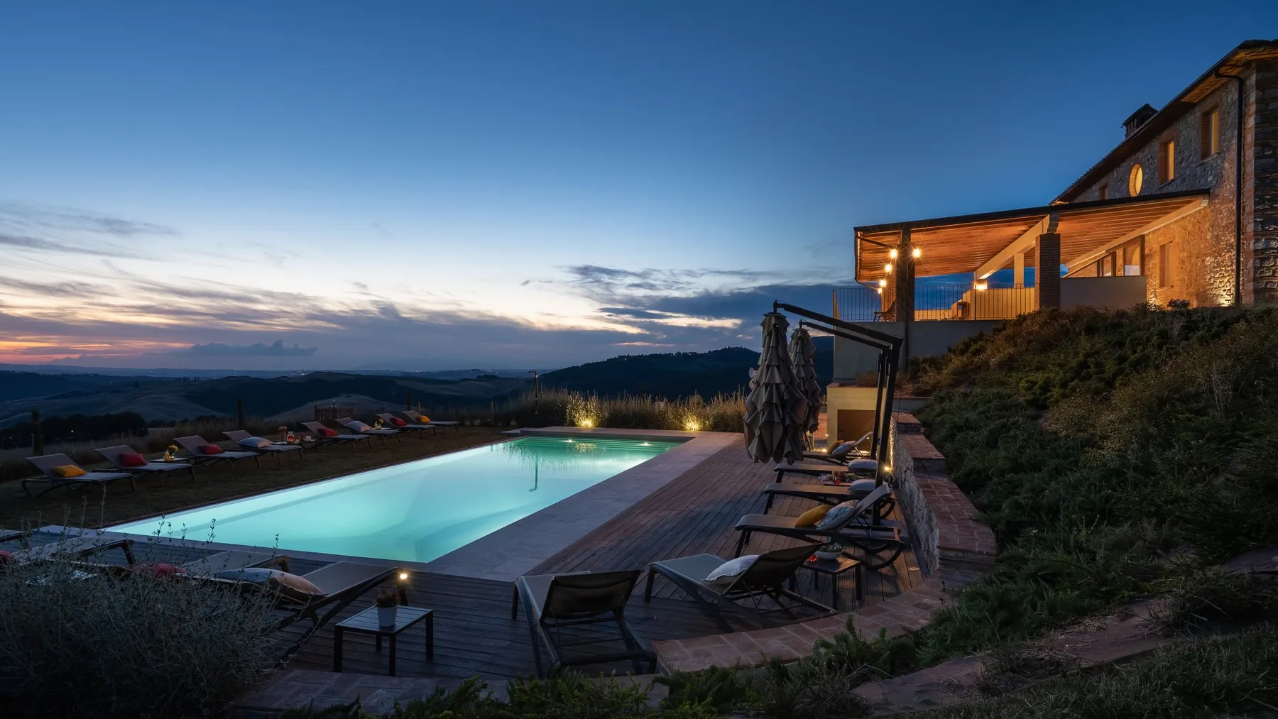 An outdoor swimming pool and surrounding deck overlook a valley at dusk.