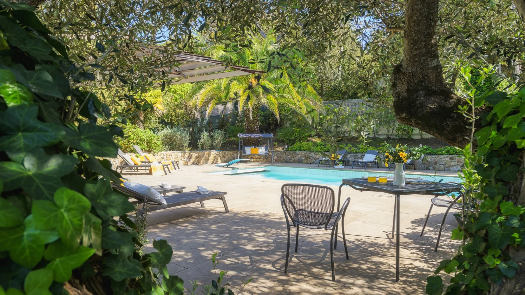 Un patio con piscina y asientos al aire libre, bajo árboles frondosos.