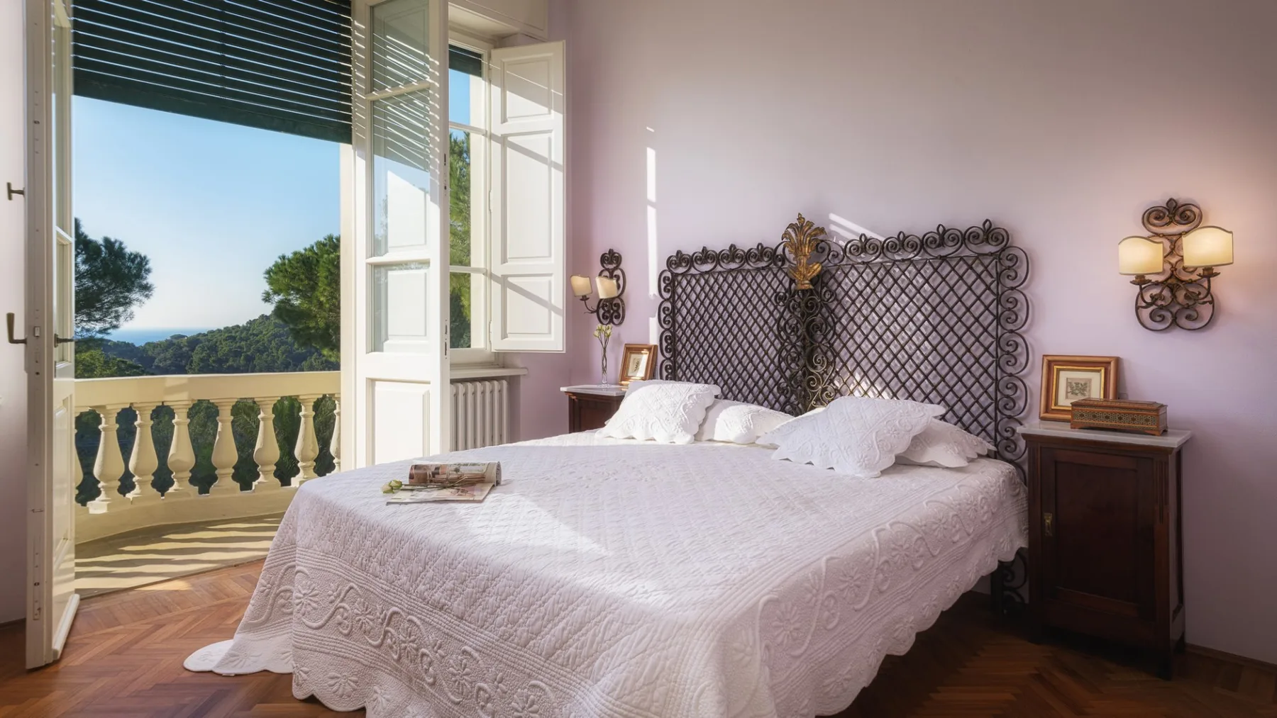 Un dormitorio con una cama junto a ventanas abiertas que dan a un paisaje verde.