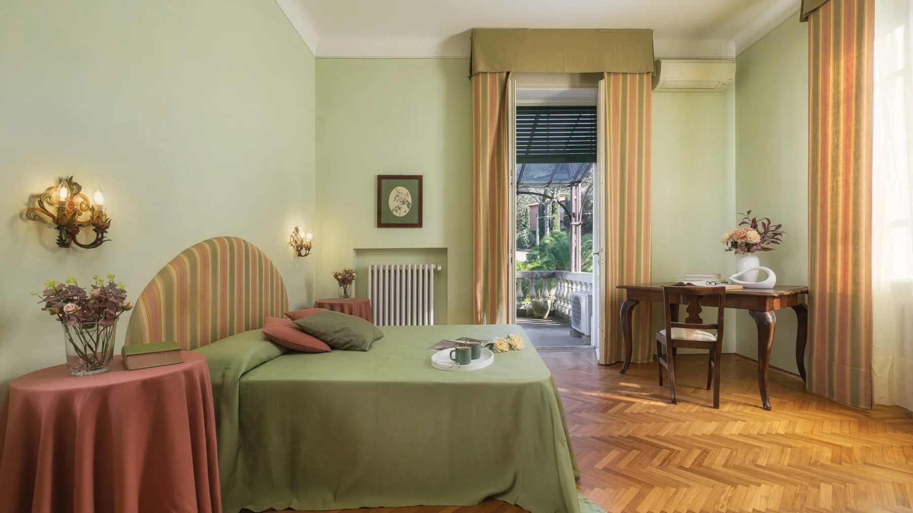 Un dormitorio con una cama cubierta de verde y una ventana alta que da a un balcón.