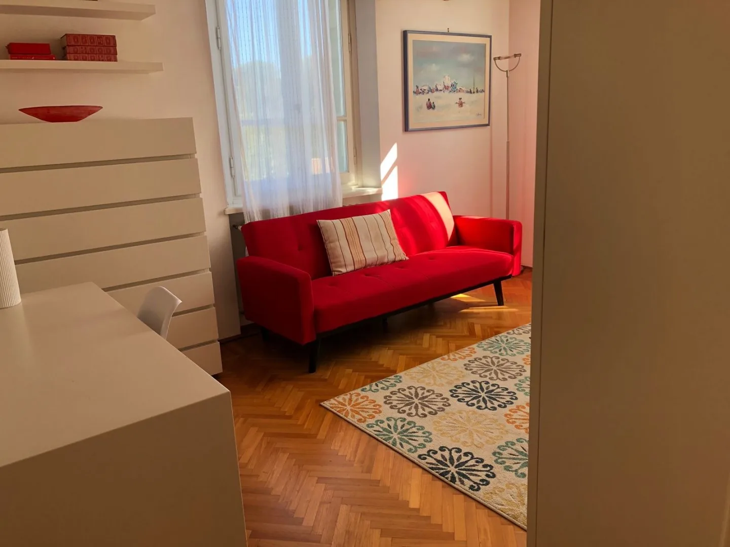 Una sala de estar con un sofá rojo junto a una ventana y una alfombra estampada.