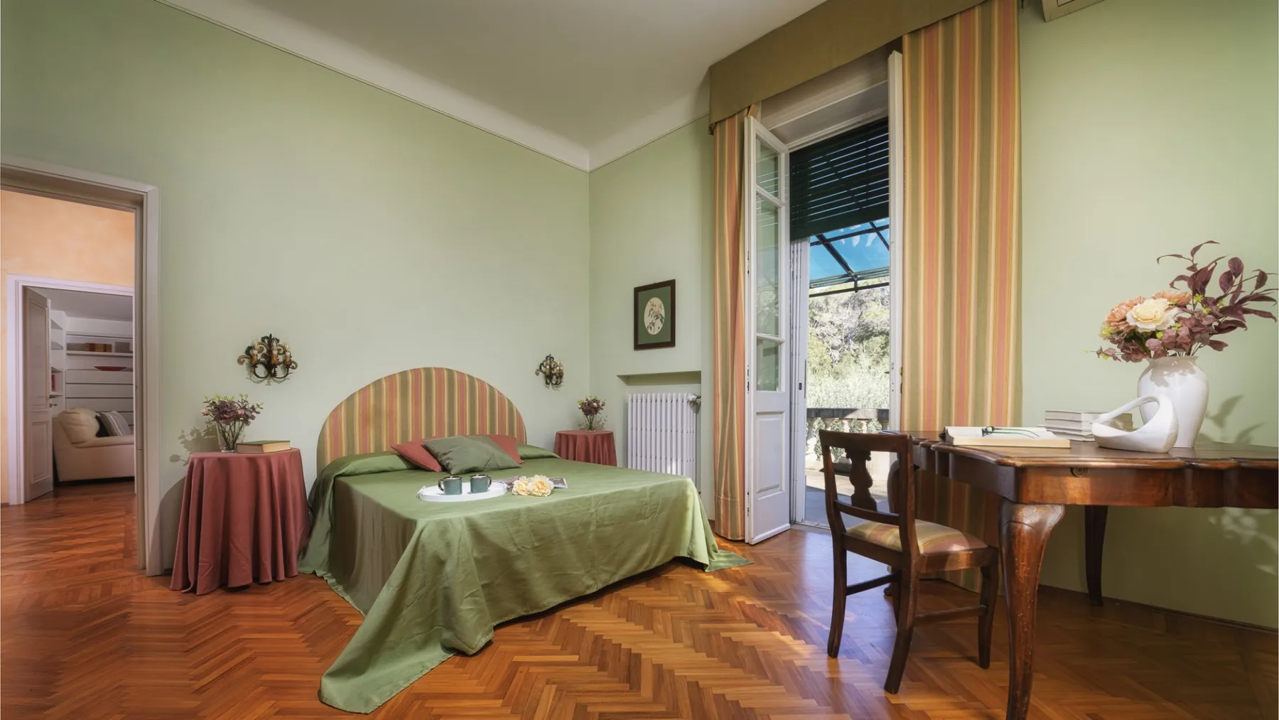 Un dormitorio con una cama, una mesa pequeña y un escritorio junto a una ventana abierta.