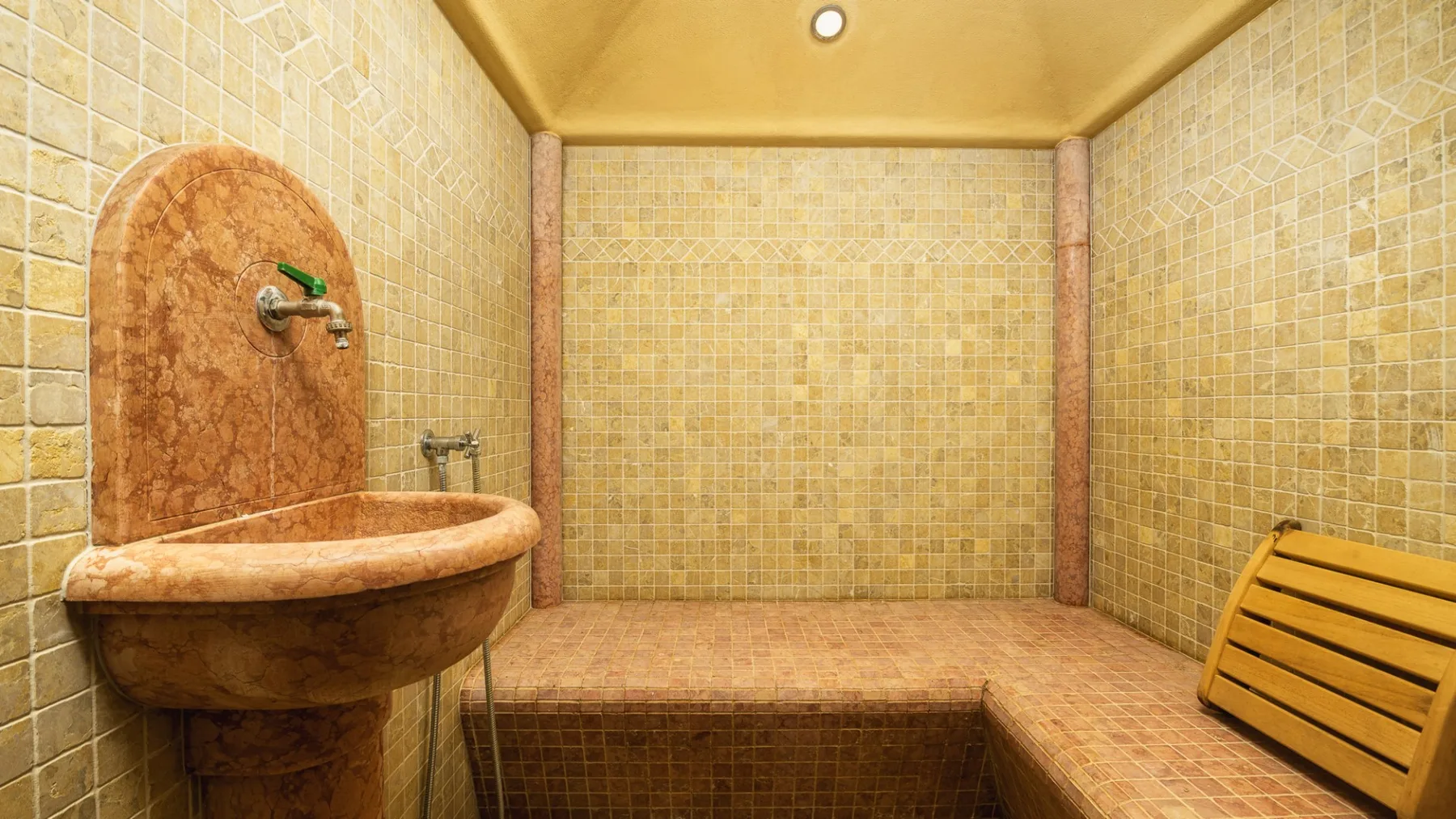 Un cuarto de baño alicatado con un lavabo integrado y un asiento de listones de madera.