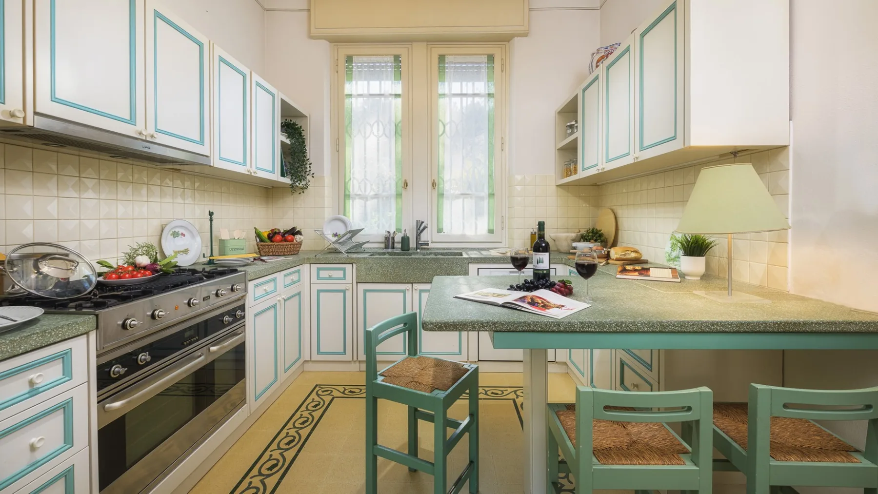 Una cocina luminosa con gabinetes de bordes verdes y una mesa central.