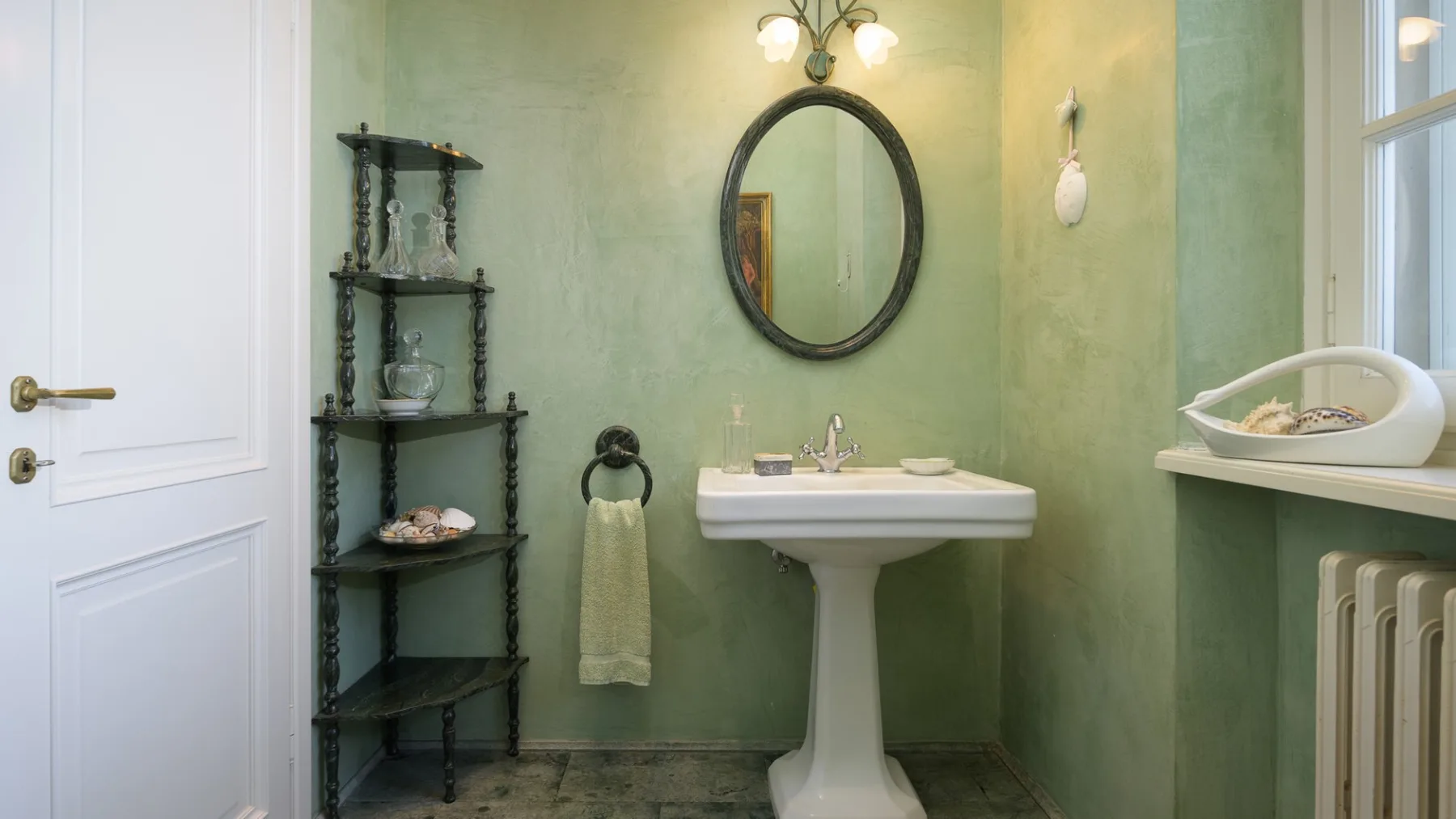 Un baño verde con lavabo de pedestal, espejo ovalado y bañera.