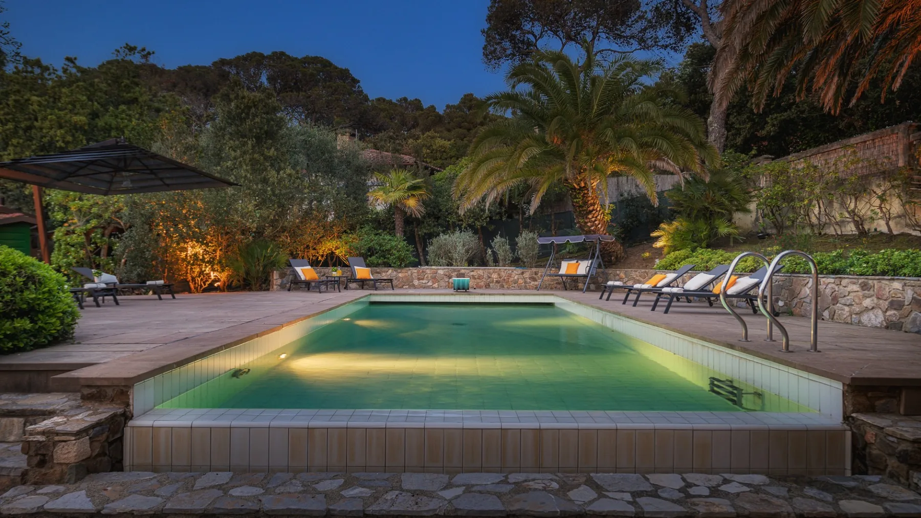Una piscina al aire libre está rodeada por un patio de piedra y tumbonas.