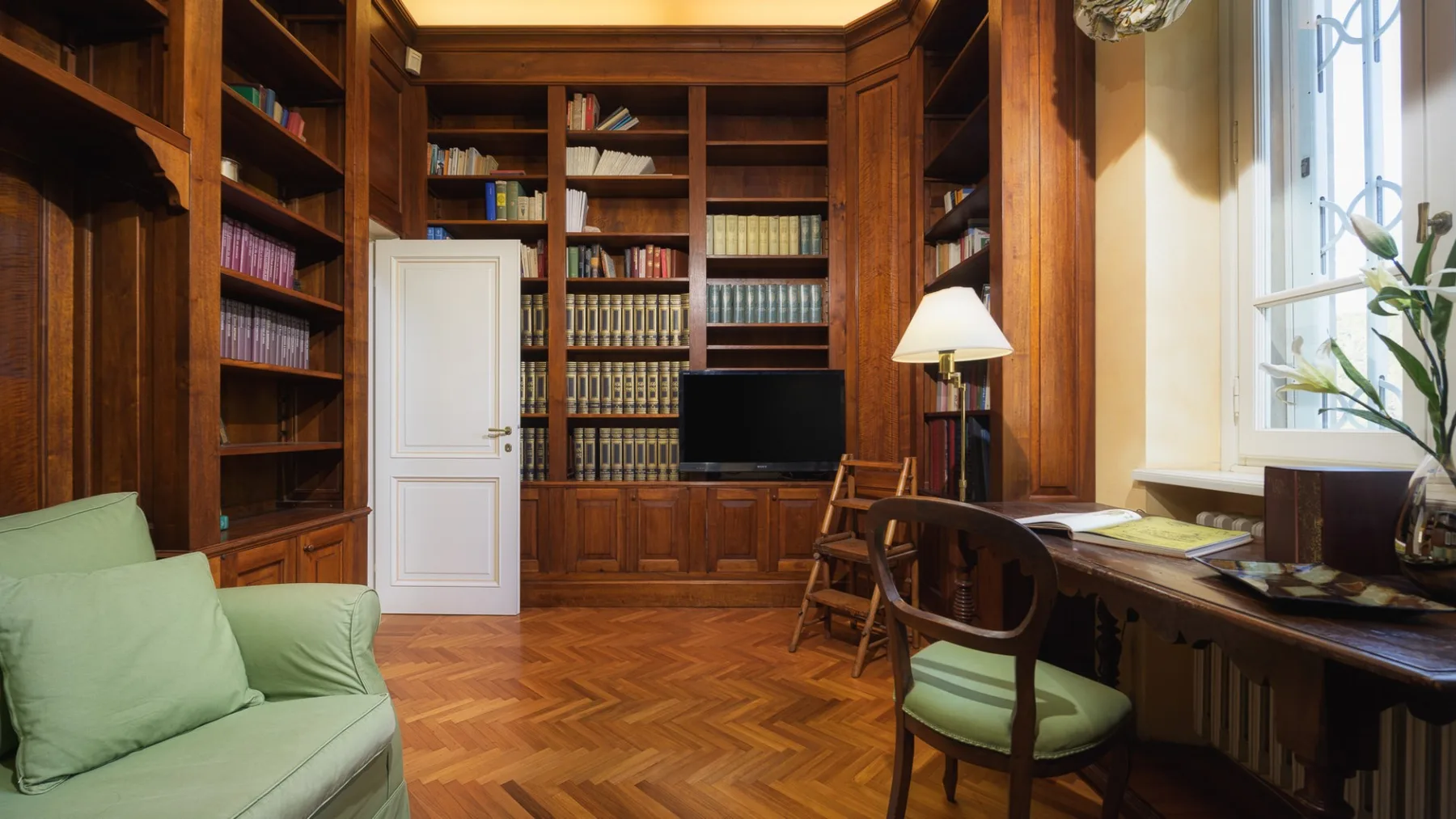 Un estudio revestido de madera con estanterías empotradas, un escritorio y asientos verdes.