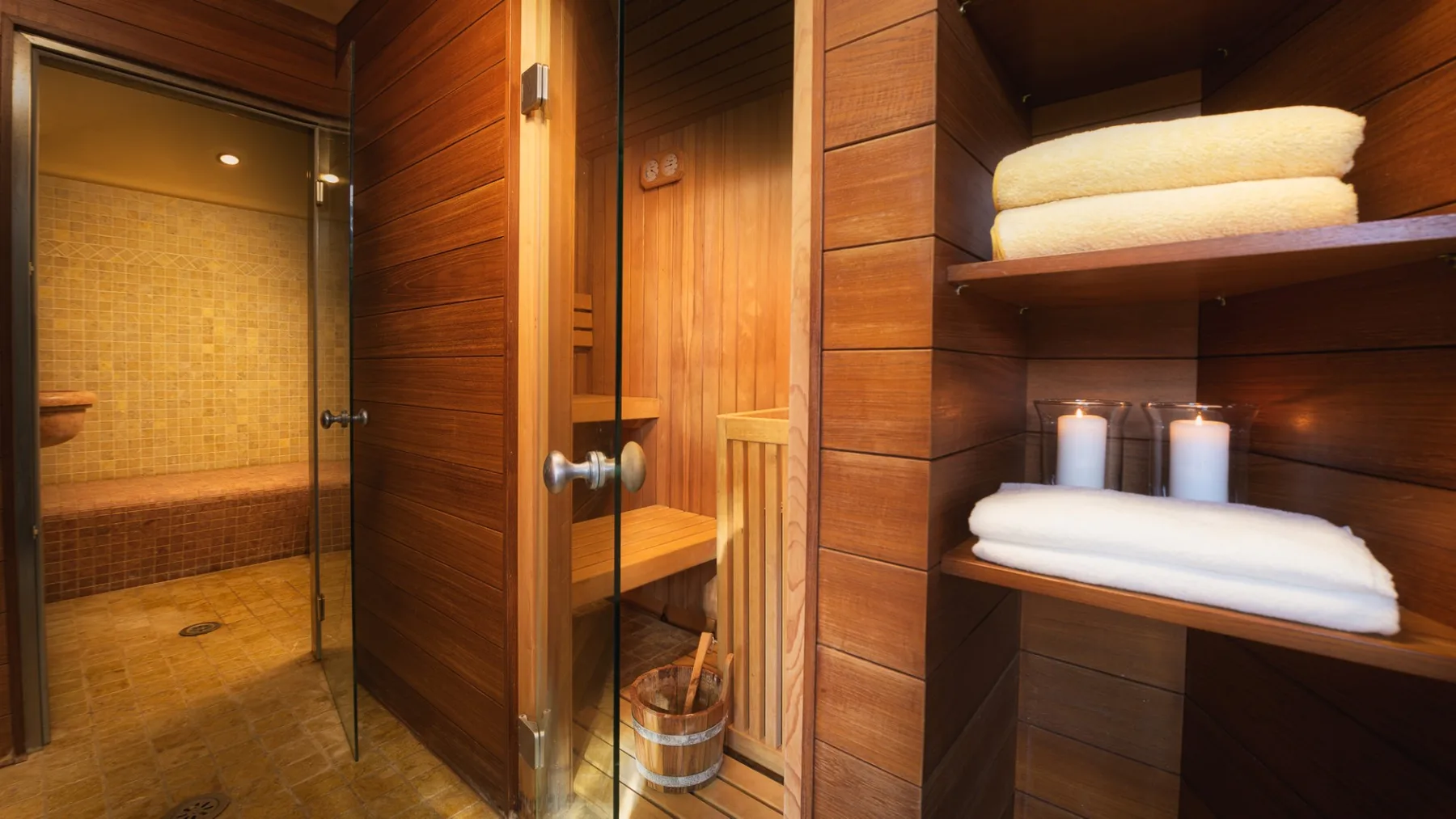 Una sauna revestida de madera con puerta de vidrio y toallas dobladas en estantes.