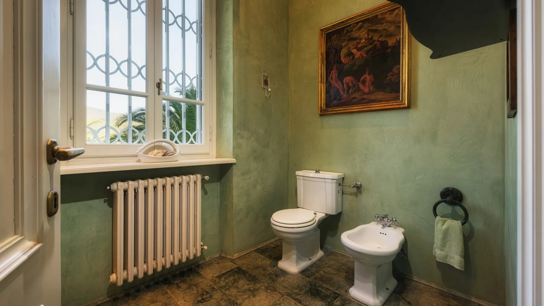 Un baño verde con inodoro, lavabo con pedestal y una ventana sobre un radiador.