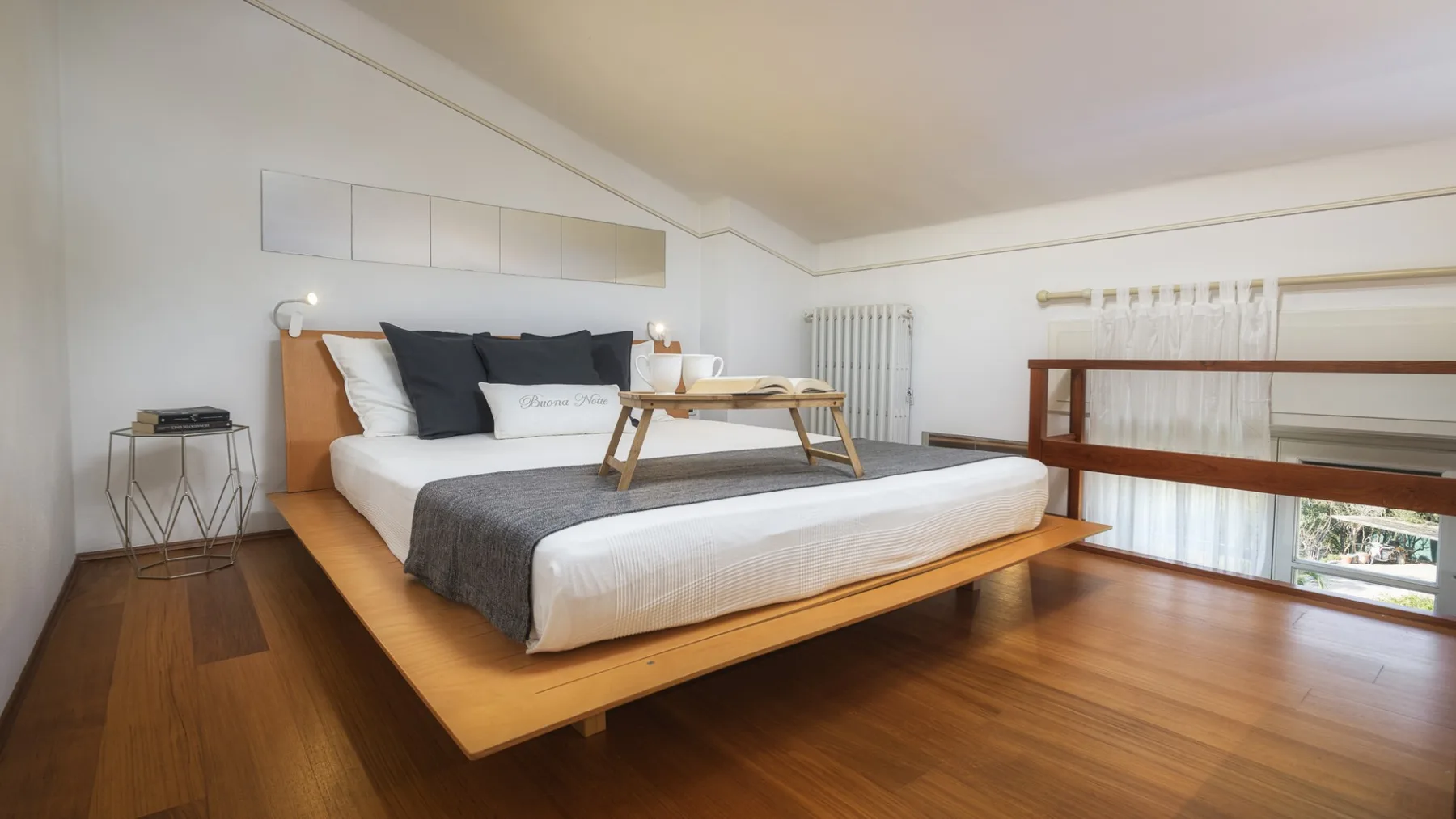 Un dormitorio con una cama baja, almohadas oscuras y suelo de madera pulida.