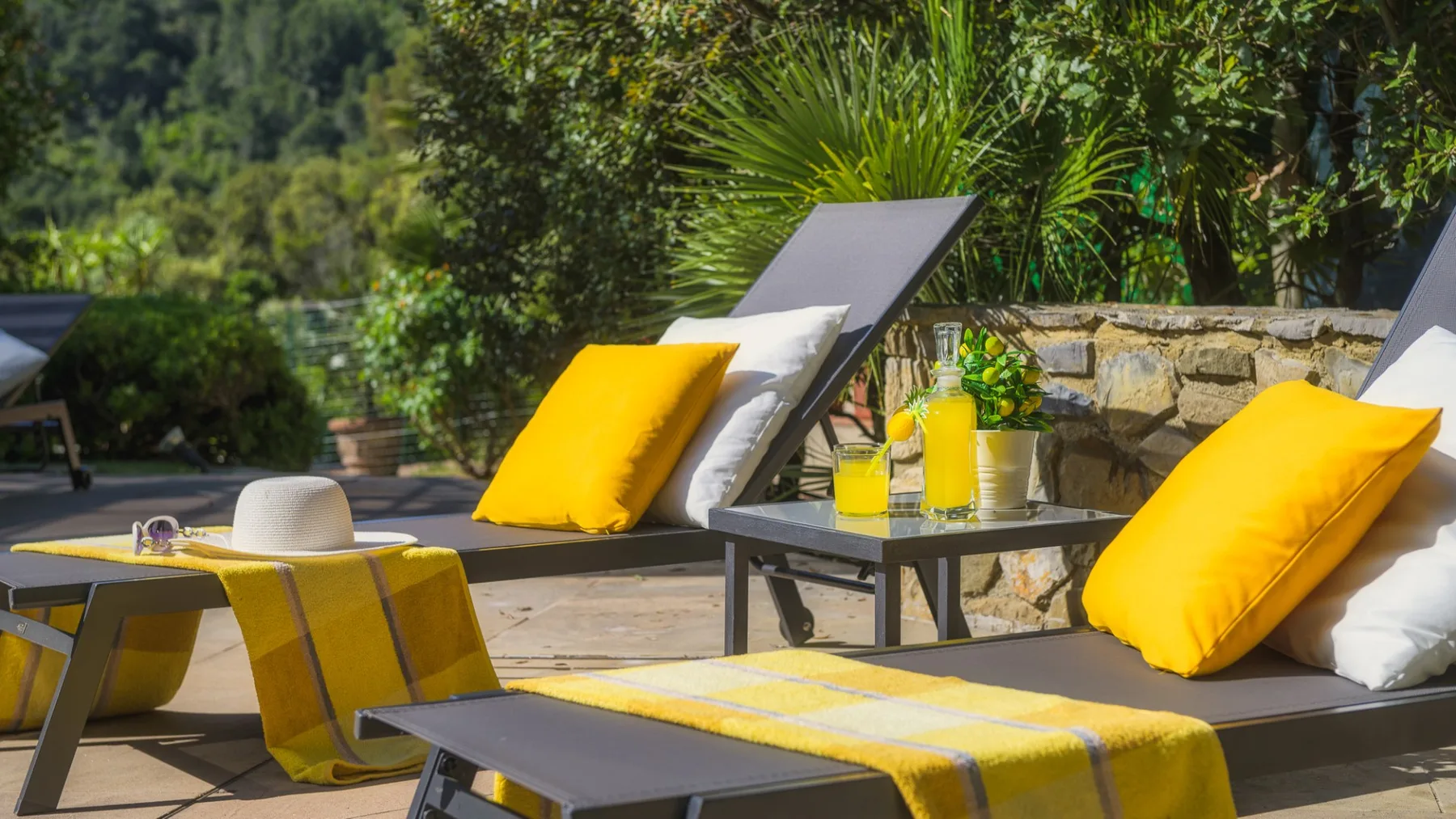 Un patio al aire libre con asientos, cojines amarillos y una mesa baja.