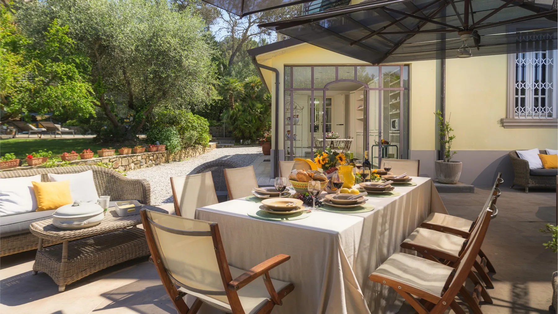 Un patio comedor al aire libre con una mesa puesta bajo una zona de estar cubierta.