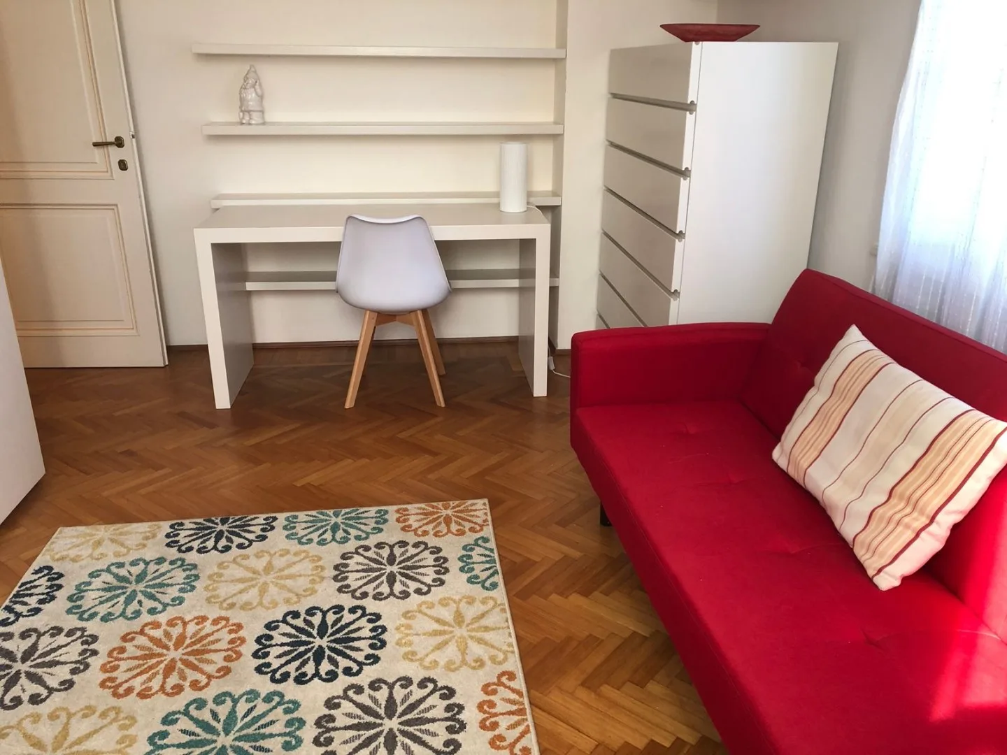 Una zona de estar con asientos rojos, un escritorio y una alfombra estampada.