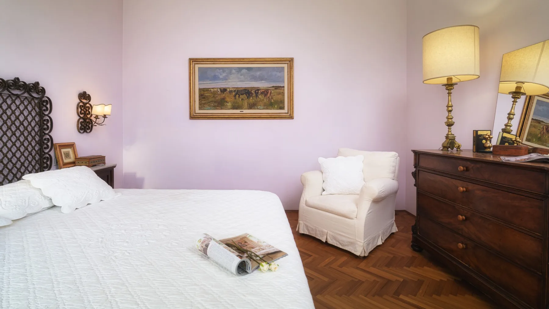 Un dormitorio con una cama, un sillón y una cómoda junto a paredes claras.