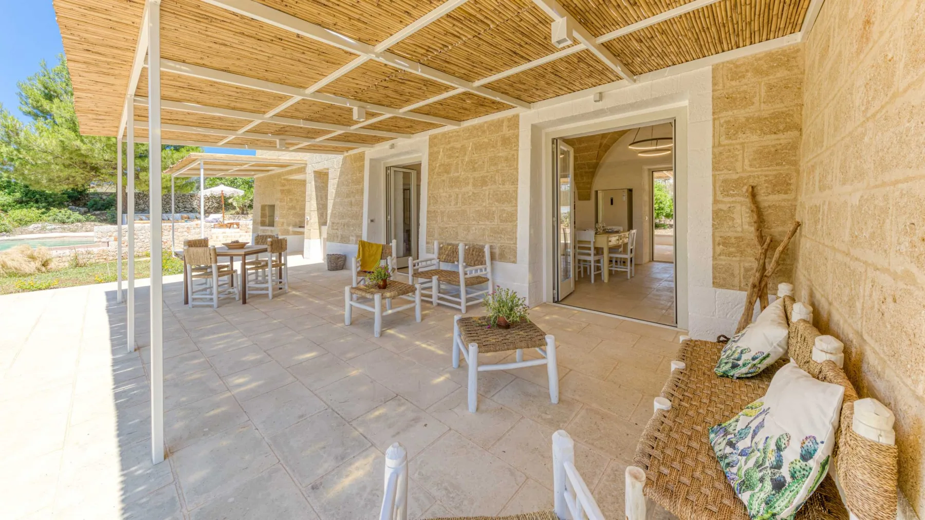 Un patio exterior cubierto con mesa de comedor y asientos junto a puertas abiertas.