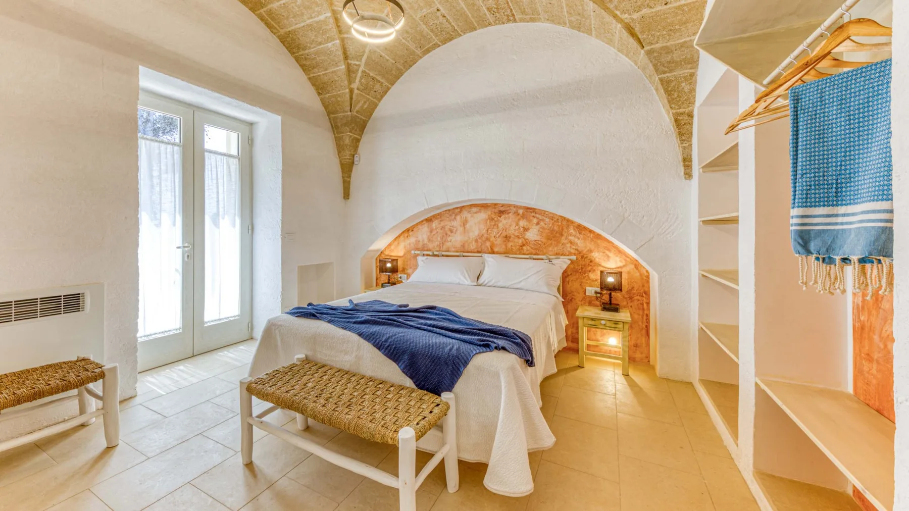 Un dormitorio con una cama bajo un techo de piedra curvo y una ventana luminosa.