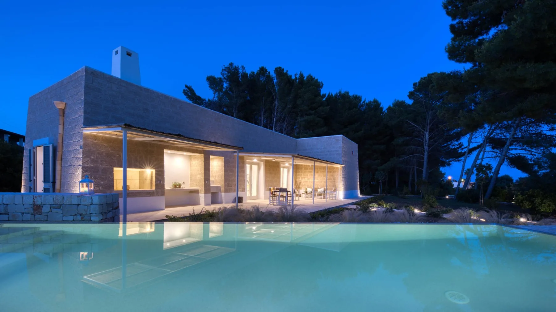 Una casa moderna junto a una piscina al anochecer.