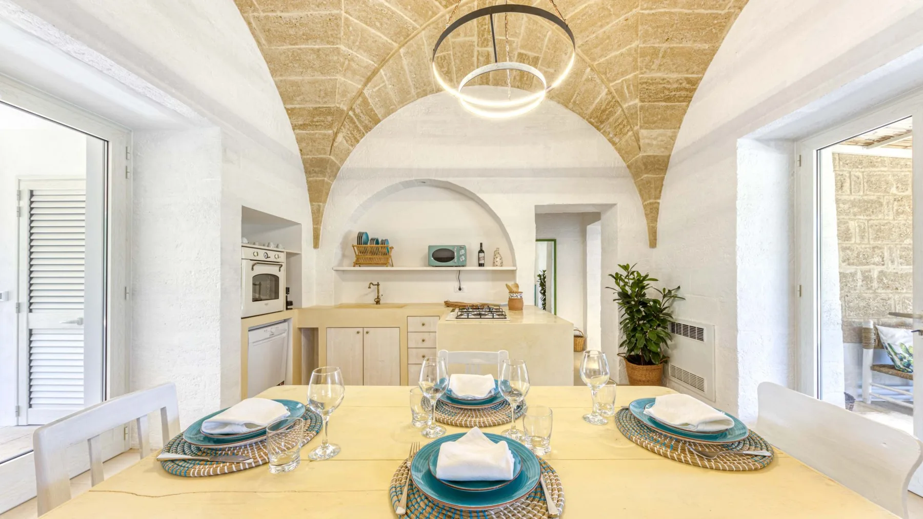 Comedor con una mesa puesta junto a una cocina compacta bajo un techo abovedado de piedra.