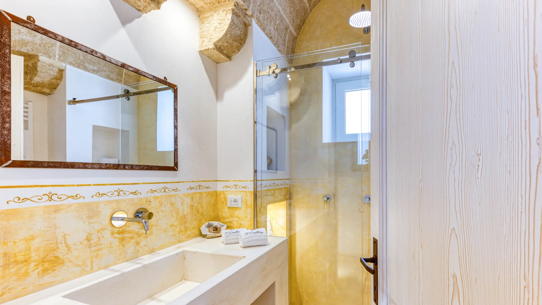 Un baño con un lavabo largo, un espejo de pared y una ducha de vidrio.