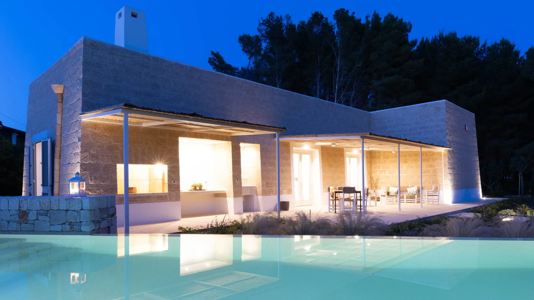 Casa moderna al anochecer con un patio iluminado junto a una piscina.