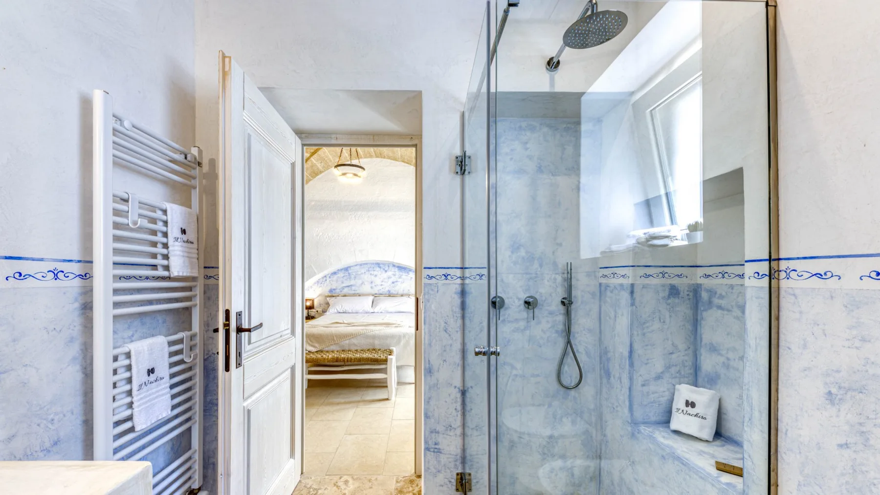 Un baño con una ducha de vidrio y una puerta abierta hacia un dormitorio.