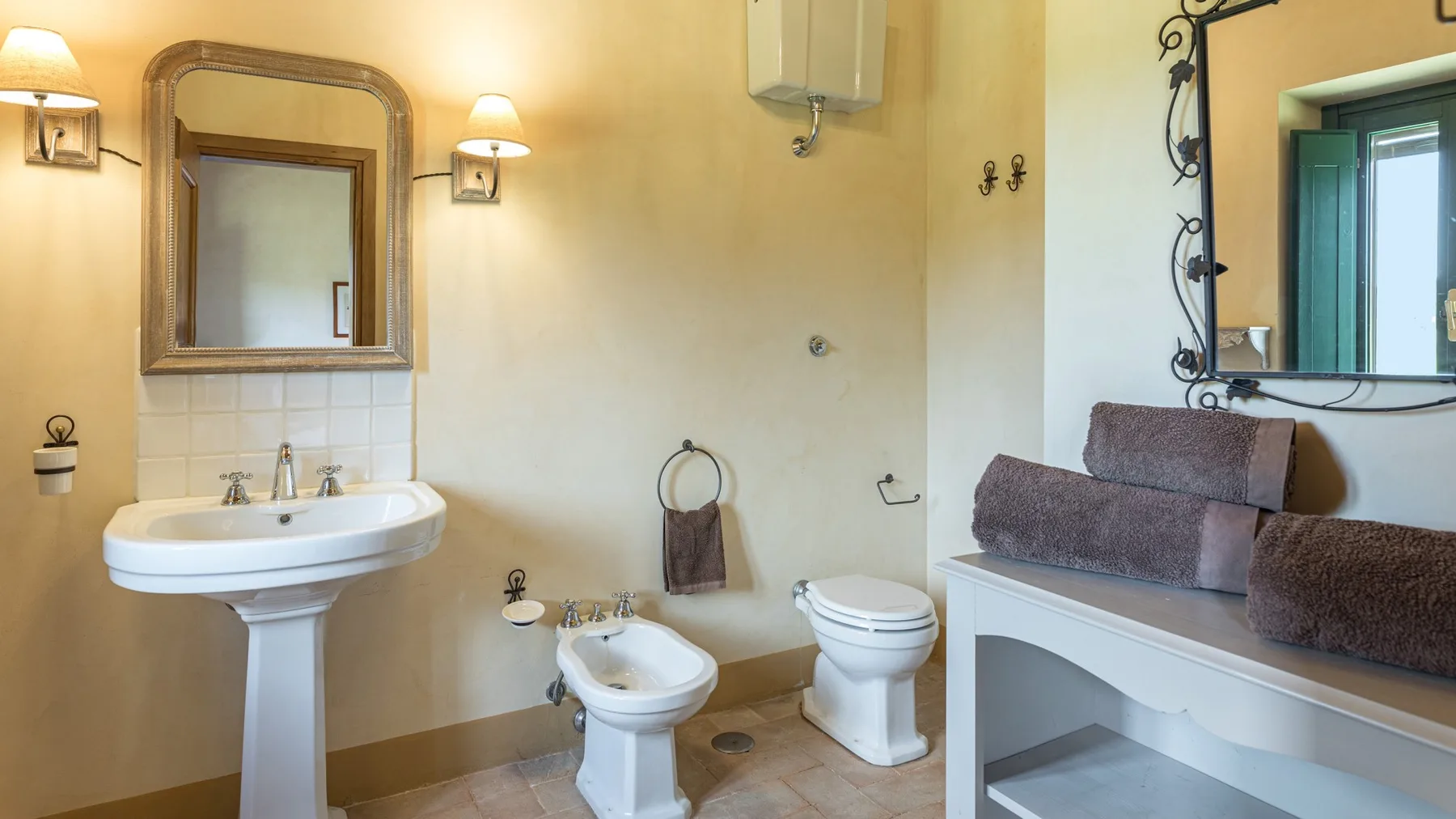 A bathroom with a sink, toilet, and a cushioned bench beneath a mirror.