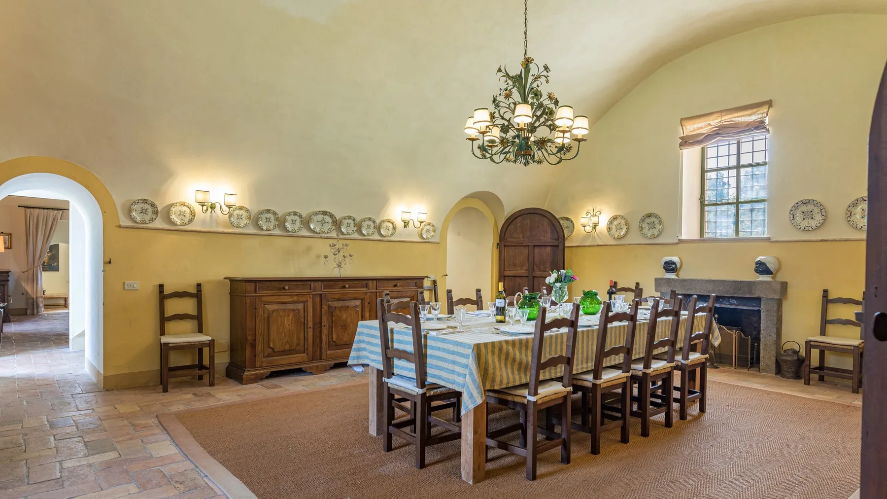 A dining room with a long table and wooden chairs beneath a chandelier.