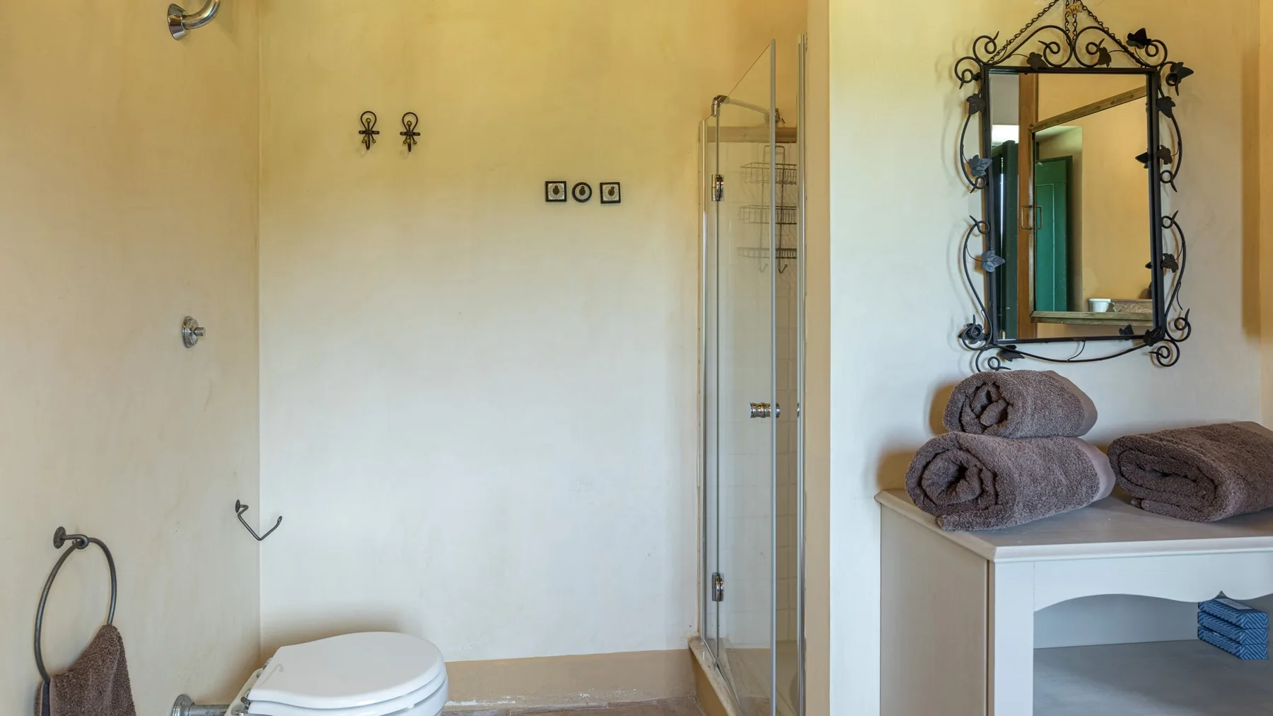 A bathroom with a toilet, glass shower, and towels beside a mirror.