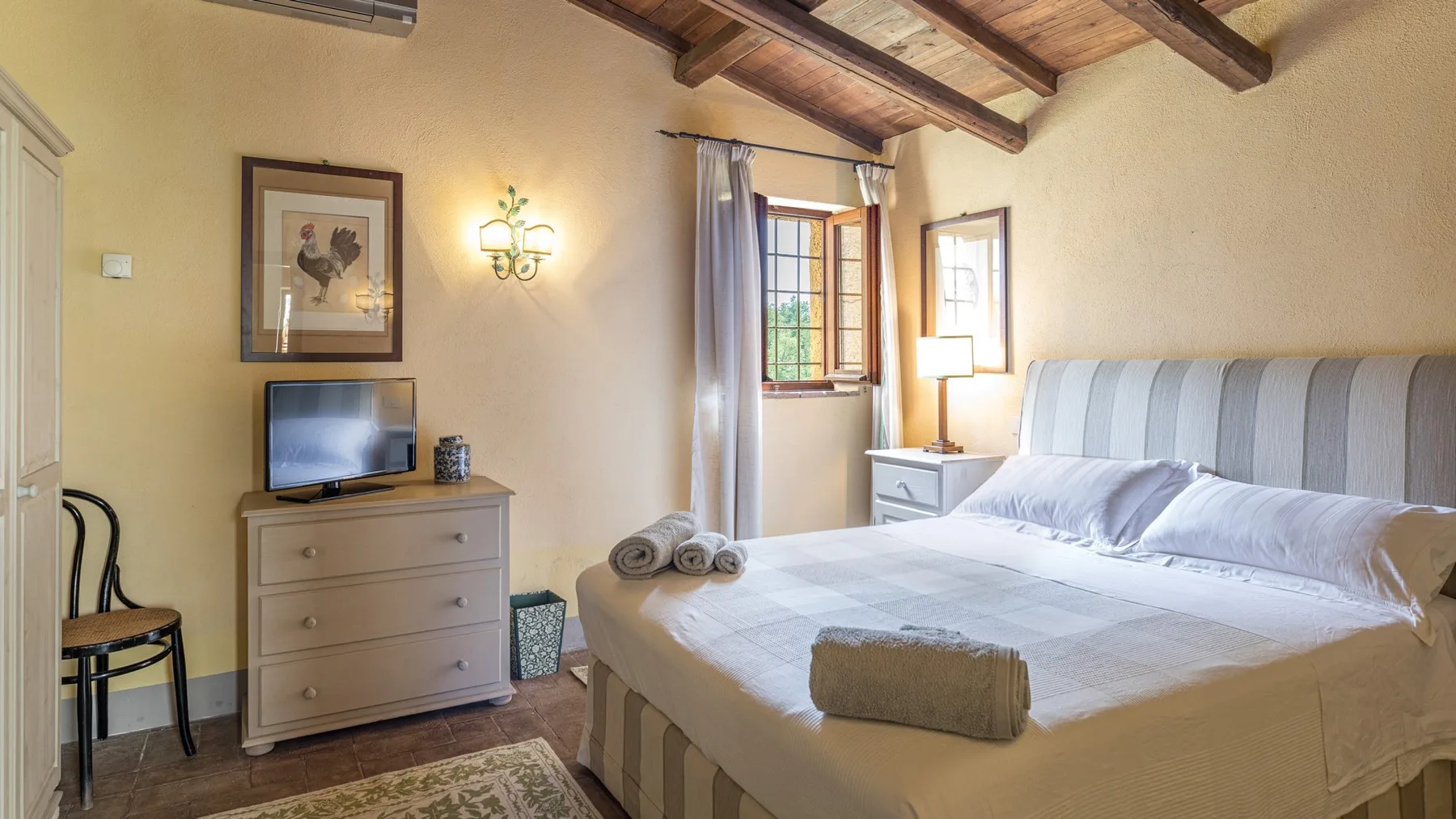 A bedroom with a neatly made bed and a wooden-beam ceiling.
