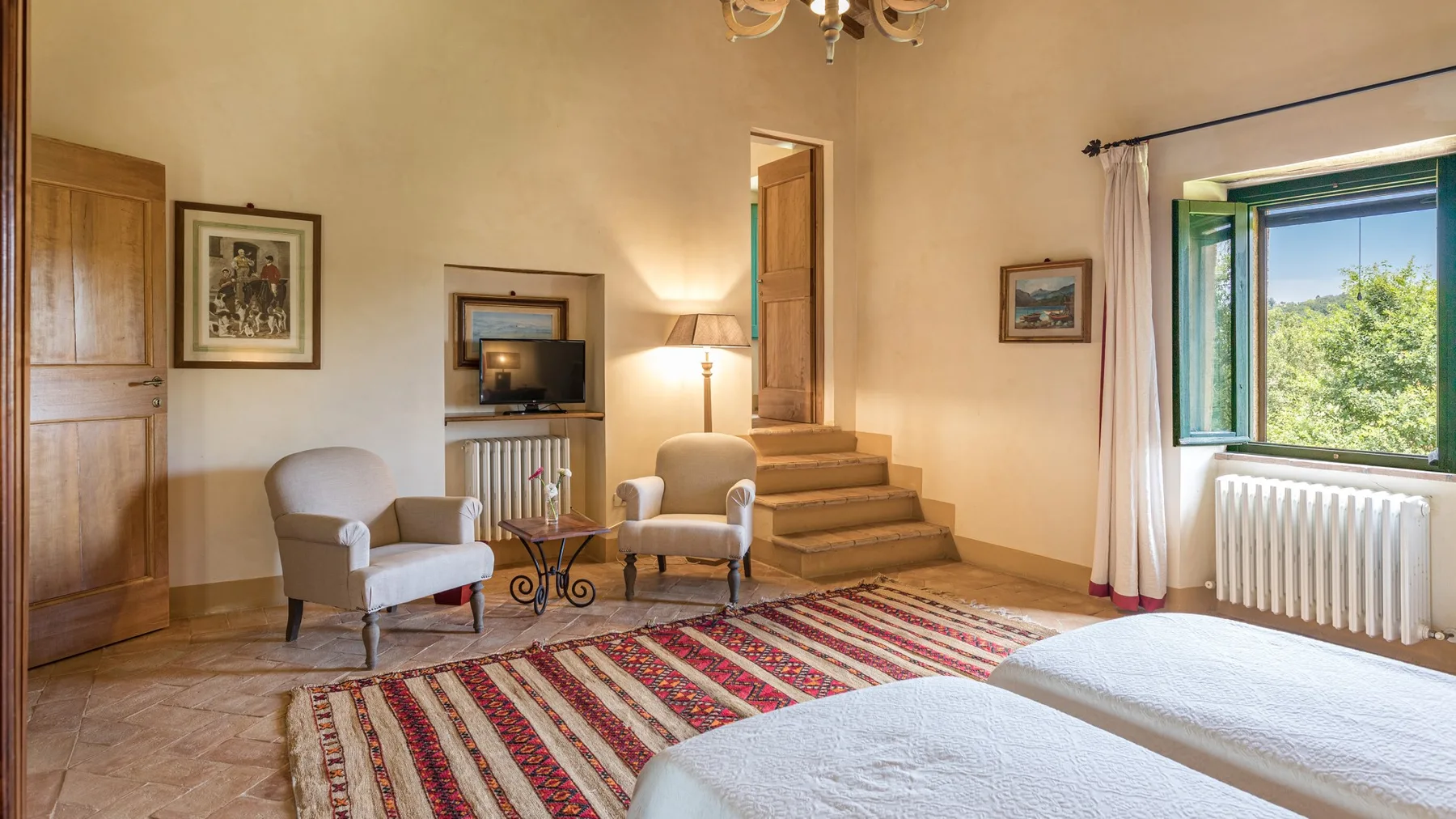 A bedroom with two seating chairs, a television, and a large patterned rug.