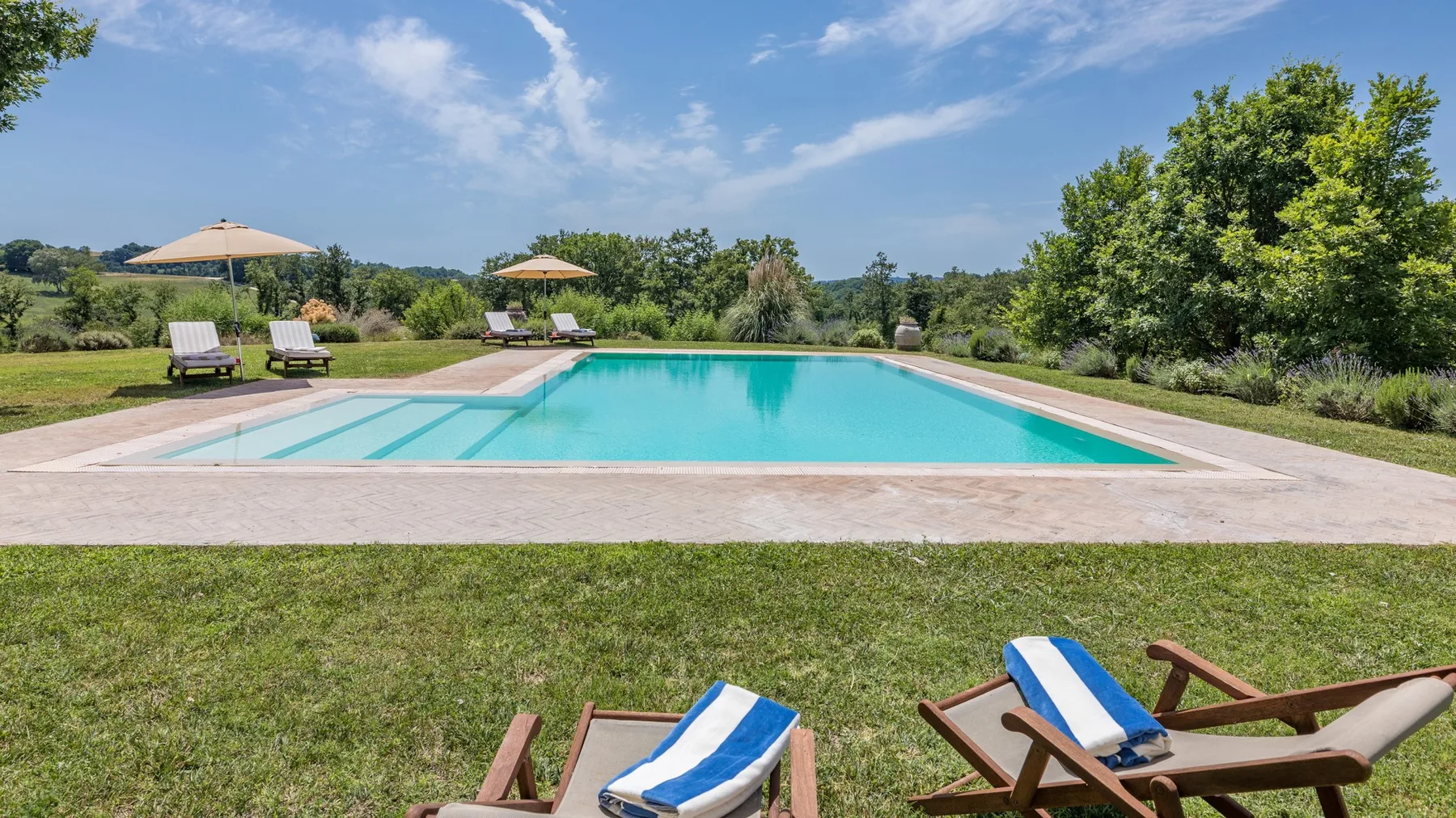 An outdoor swimming pool sits beside a grassy lawn with loungers and umbrellas.